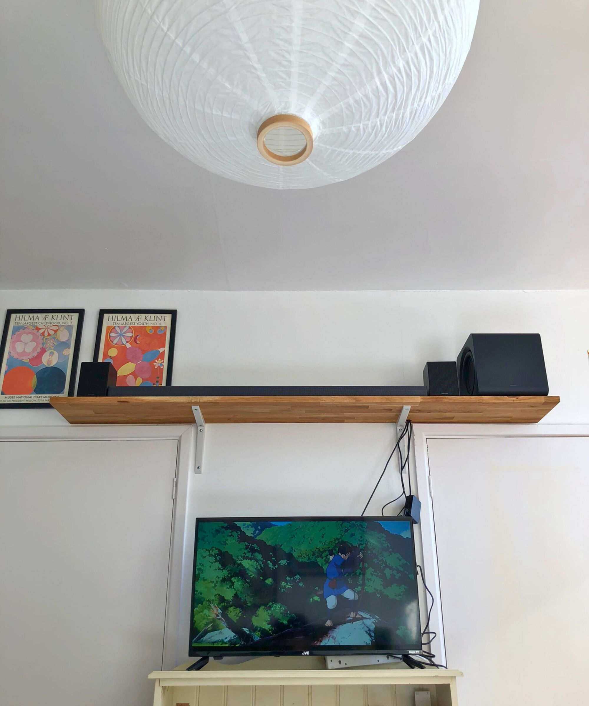 Samsung HW-QS750F soundbar on wooden shelf in Dan Fauzi's home, above TV showing Princess Mononoke and with two art prints pictured to the left.