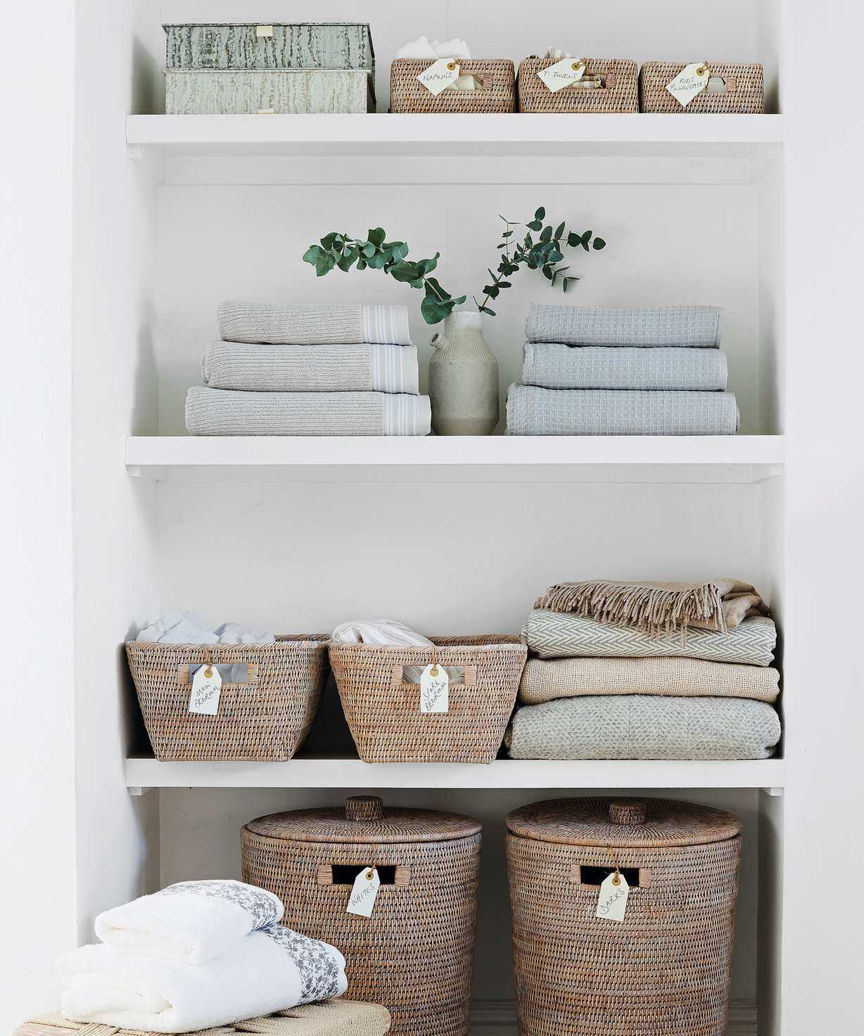 Open shelving area used for folder tidy linens, towels and blankets, along with open and closed wicker baskets that have labels on