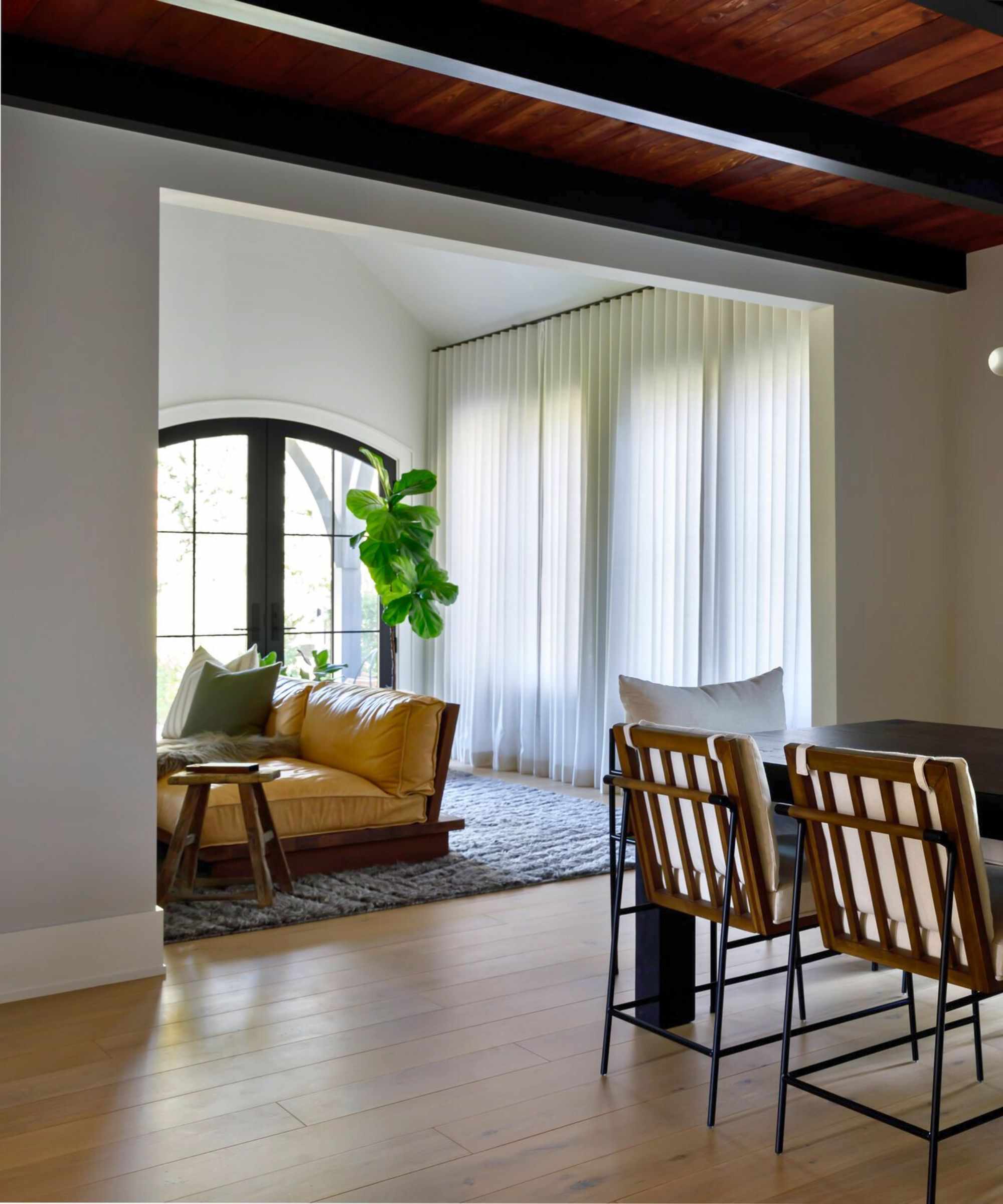 Semi-sheer net curtains in living room creating privacy for a large window. There is a butter yellow leather sectional in view, on a cozy blue-gray rug, and the corner of a chic dining table to the right in view
