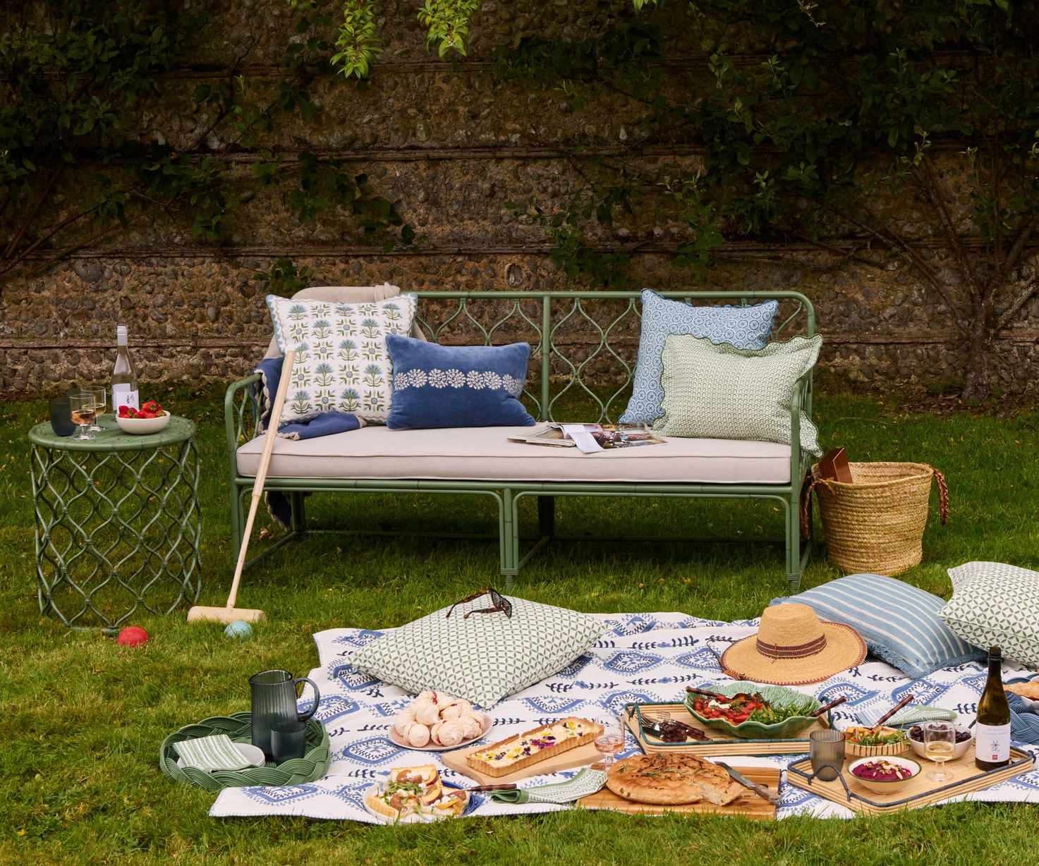 green garden sofa and side table styled with printed throw pillows with a picnic rug party spread styled on the floor