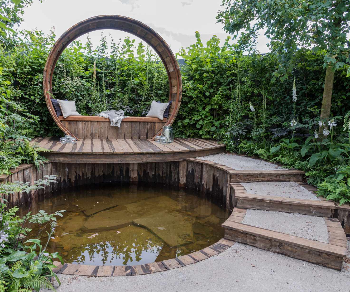 pond design with elevated deck and seating area, and path leading to it, surrounded by shrubs, trees and flowers
