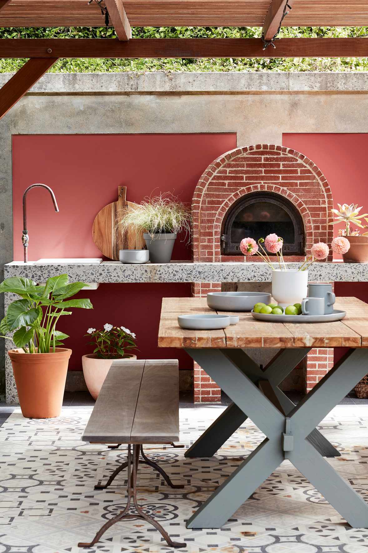 An outdoor kitchen with a brick pizza oven, sink and wooden table and bench