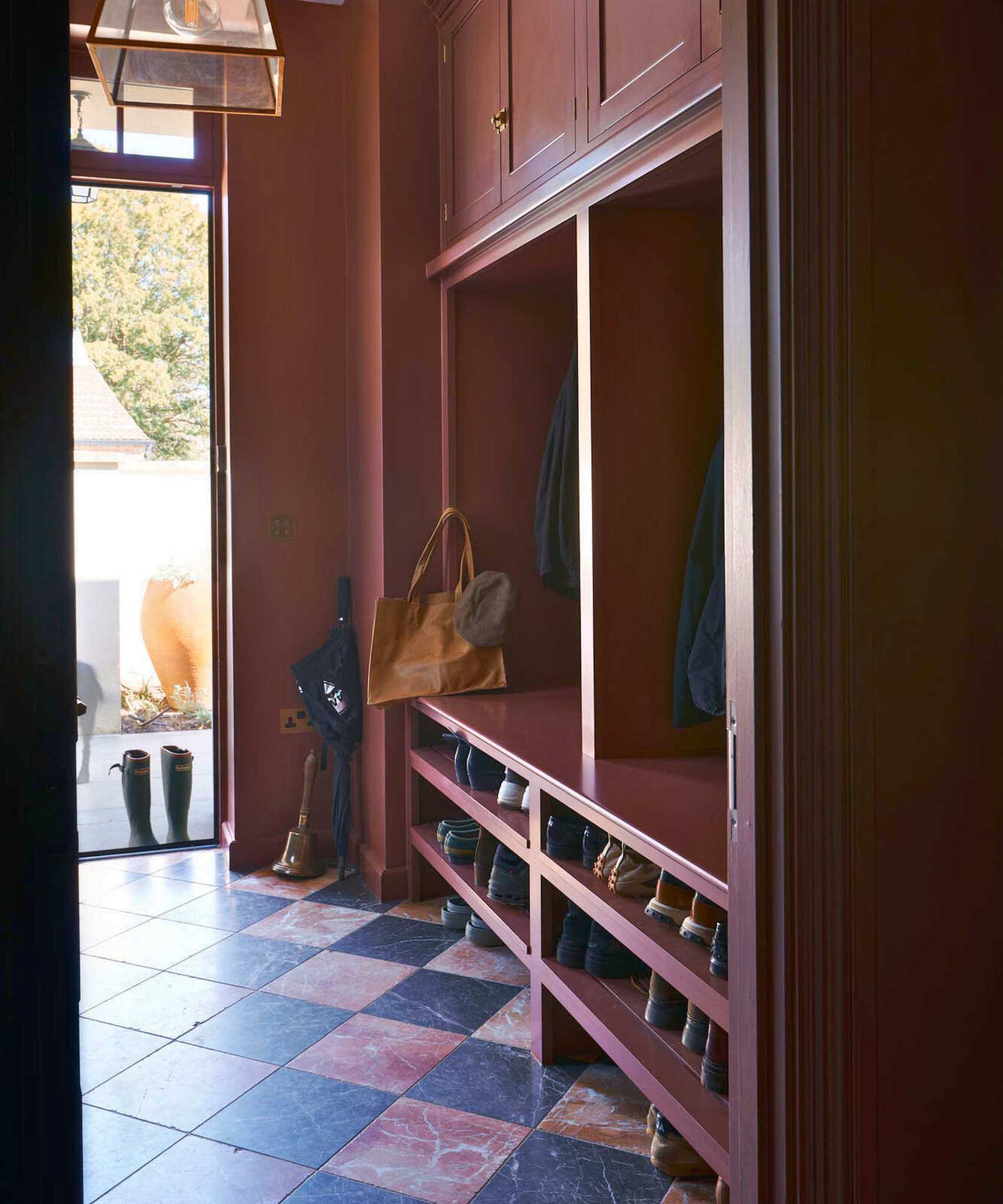 Moody burgundy boot room with marble checkered floor and built-in storage to the right, showing shoes on the lower third, vertical open cubbies for coats, and closed cabinets at the tome