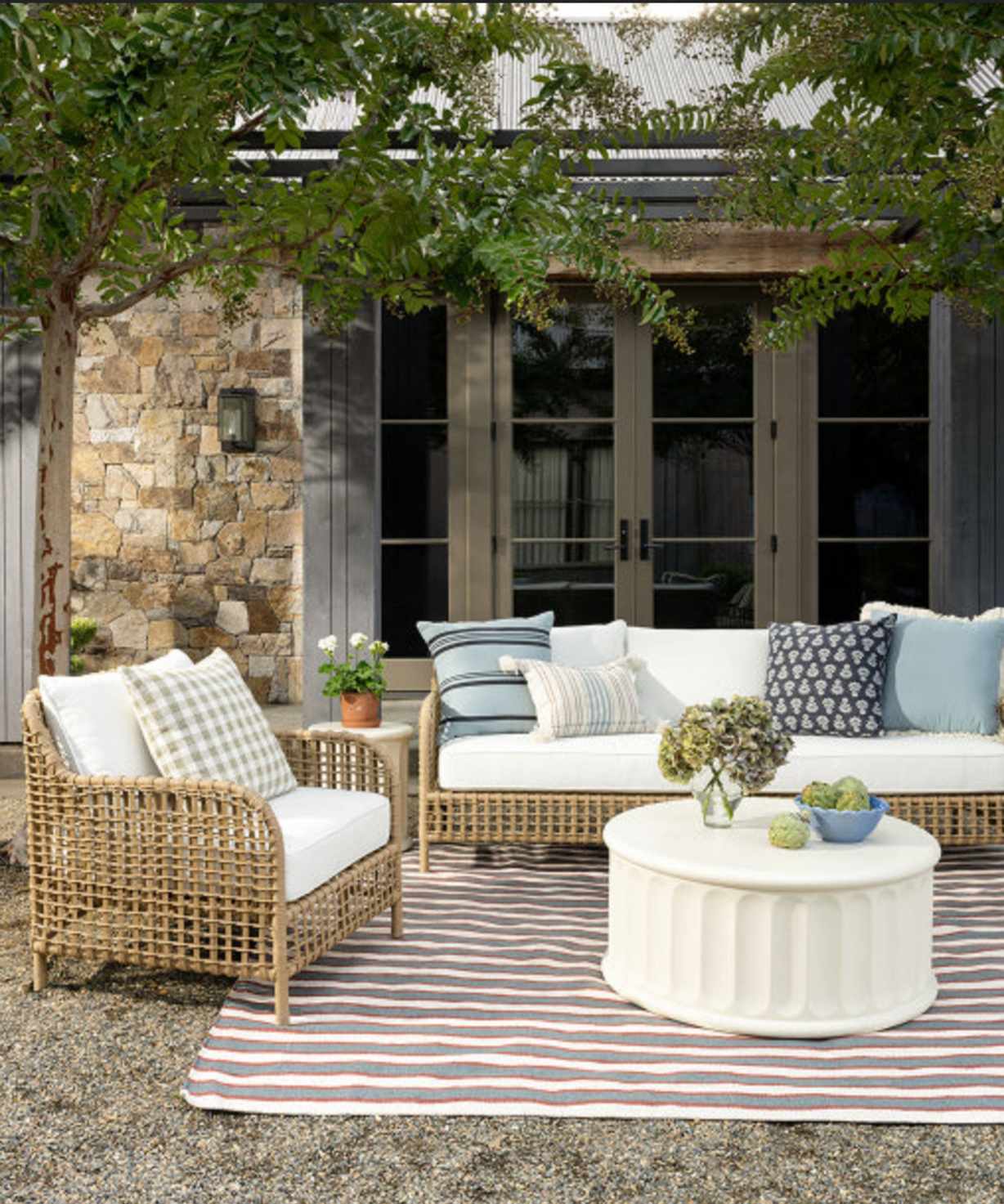 Outdoor living room with rattan furnitue, blue patterned throw pillows, a white coffee table and striped rug