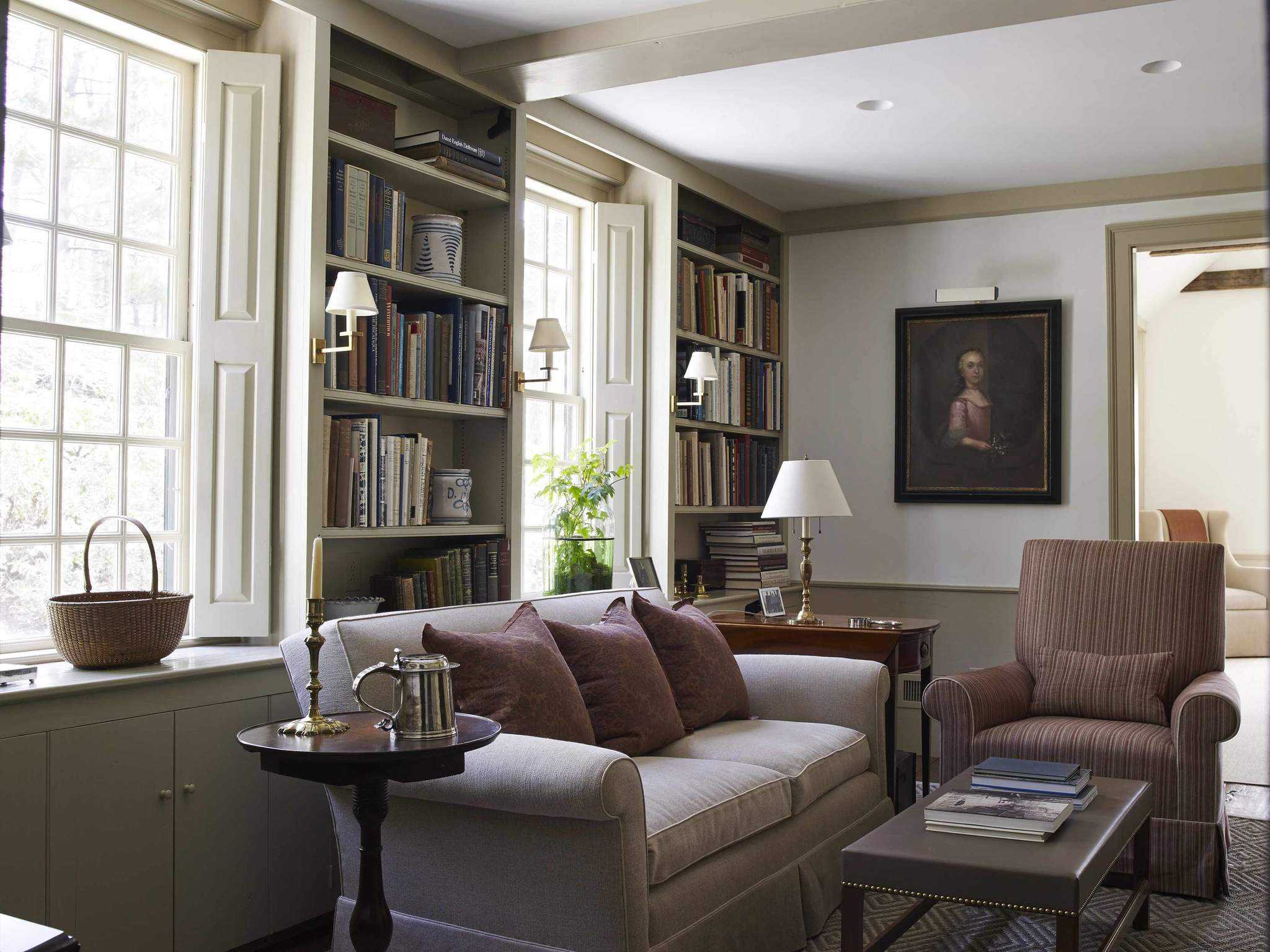 A library with custom built bookshelves and shutters and neutral walls and upholstery