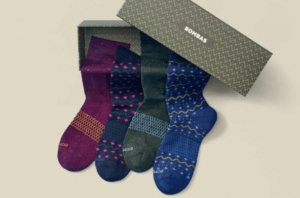 Four socks are pictured positioned on a gift box. They are burgundy, blue, green and cobalt patterened.