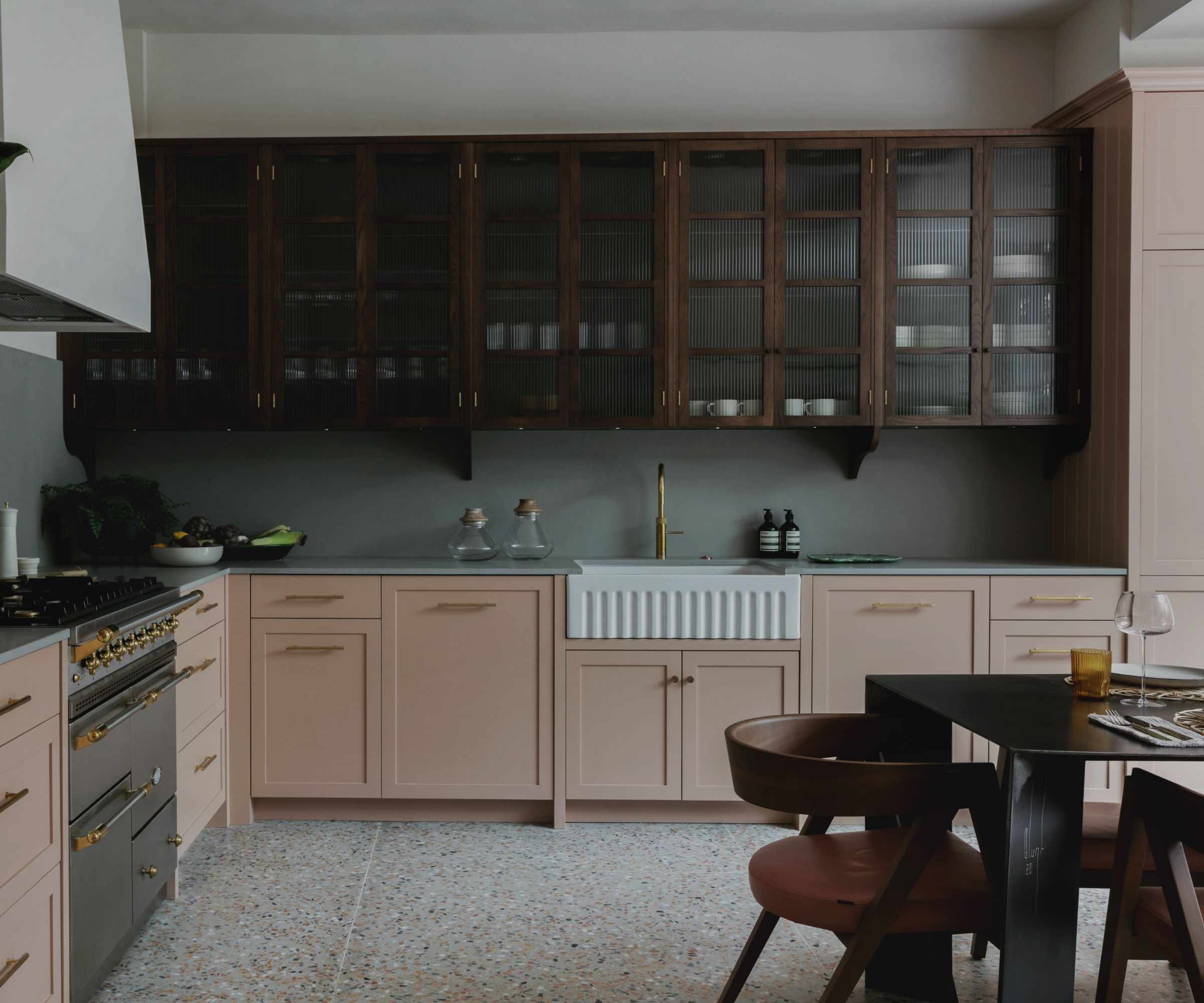 An L-shaped kitchen with pink base cabinets and glass fronted wooden upper cabinets