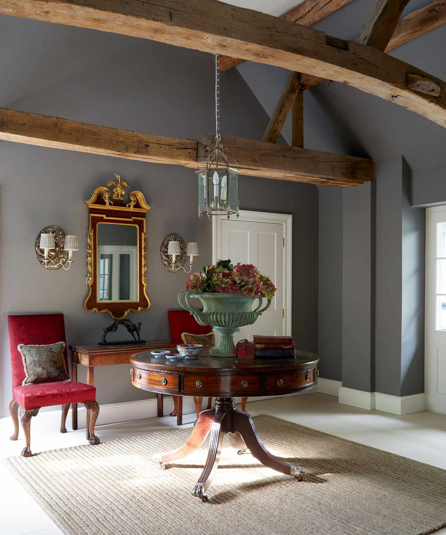 Antiques in a classic hallway idea with gray walls, round table and gilded mirror.
