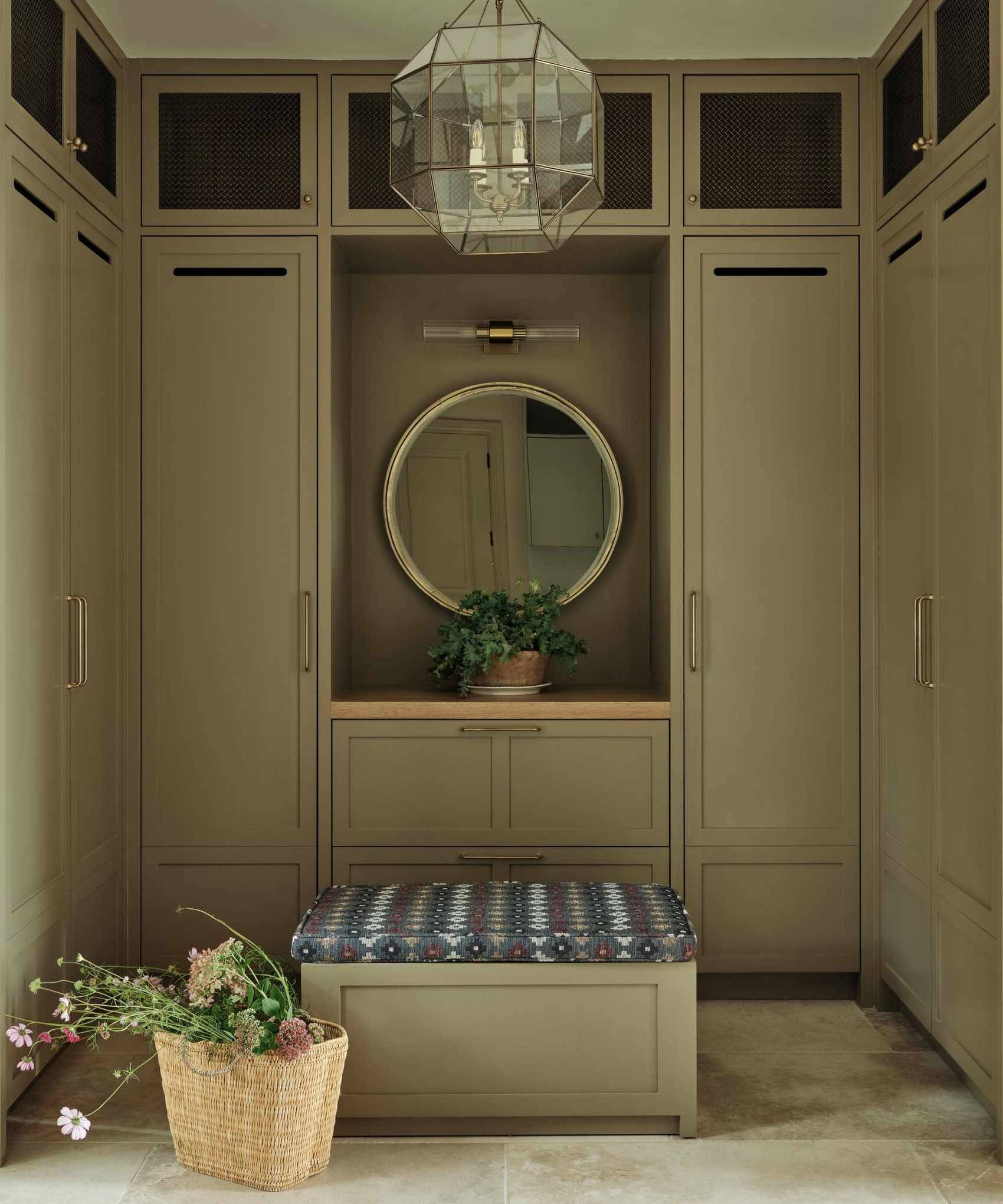 Sage green boot room with built in cabinetry and a square ottoman in the center