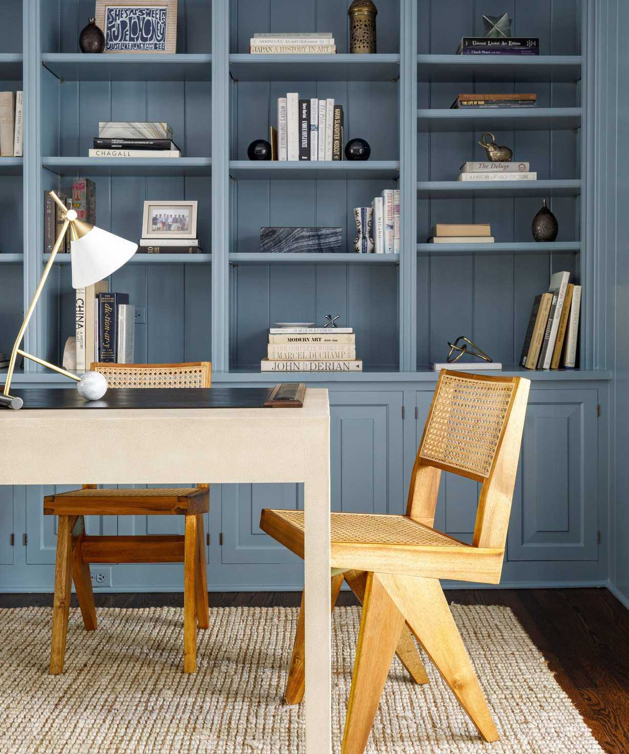 Home office with blue shelves, wooden midcentury chairs and angular table lamp