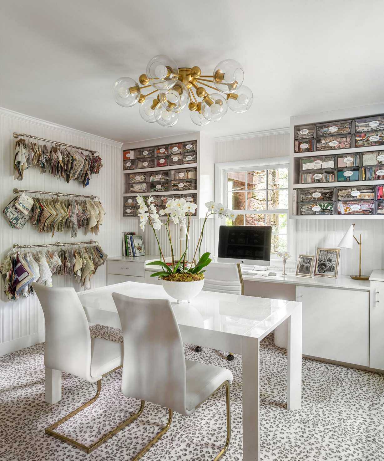 White office with patterned rug, white desk and chairs and gold statement light