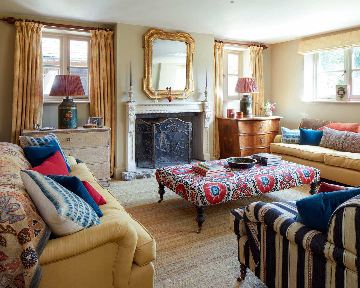Traditional living room with cozy seating, ottoman, fireplace, symmetrical design with mirrors and cabinets