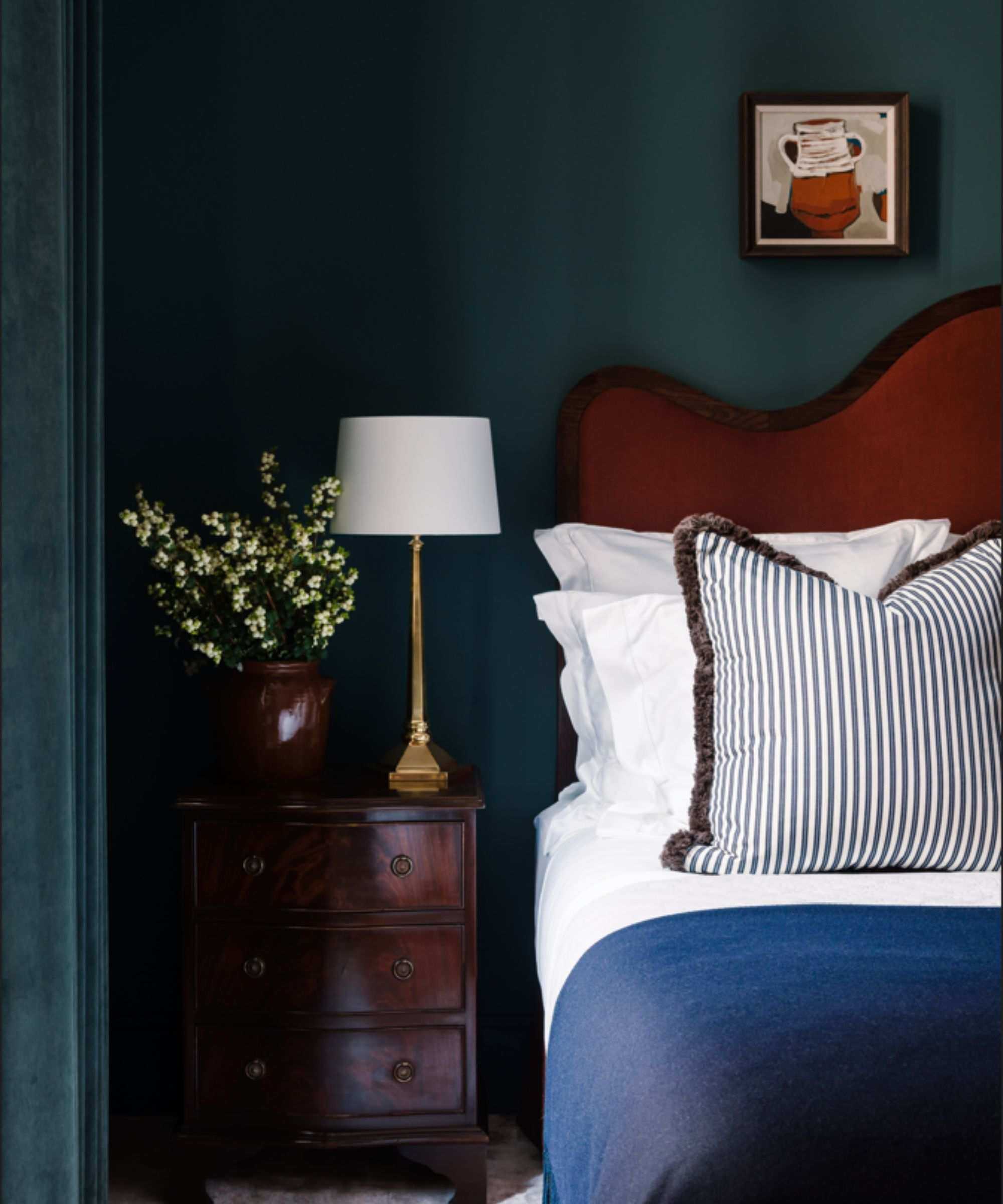 A deep blue bedroom with a red velvet bed, and a dark wood oak side table.