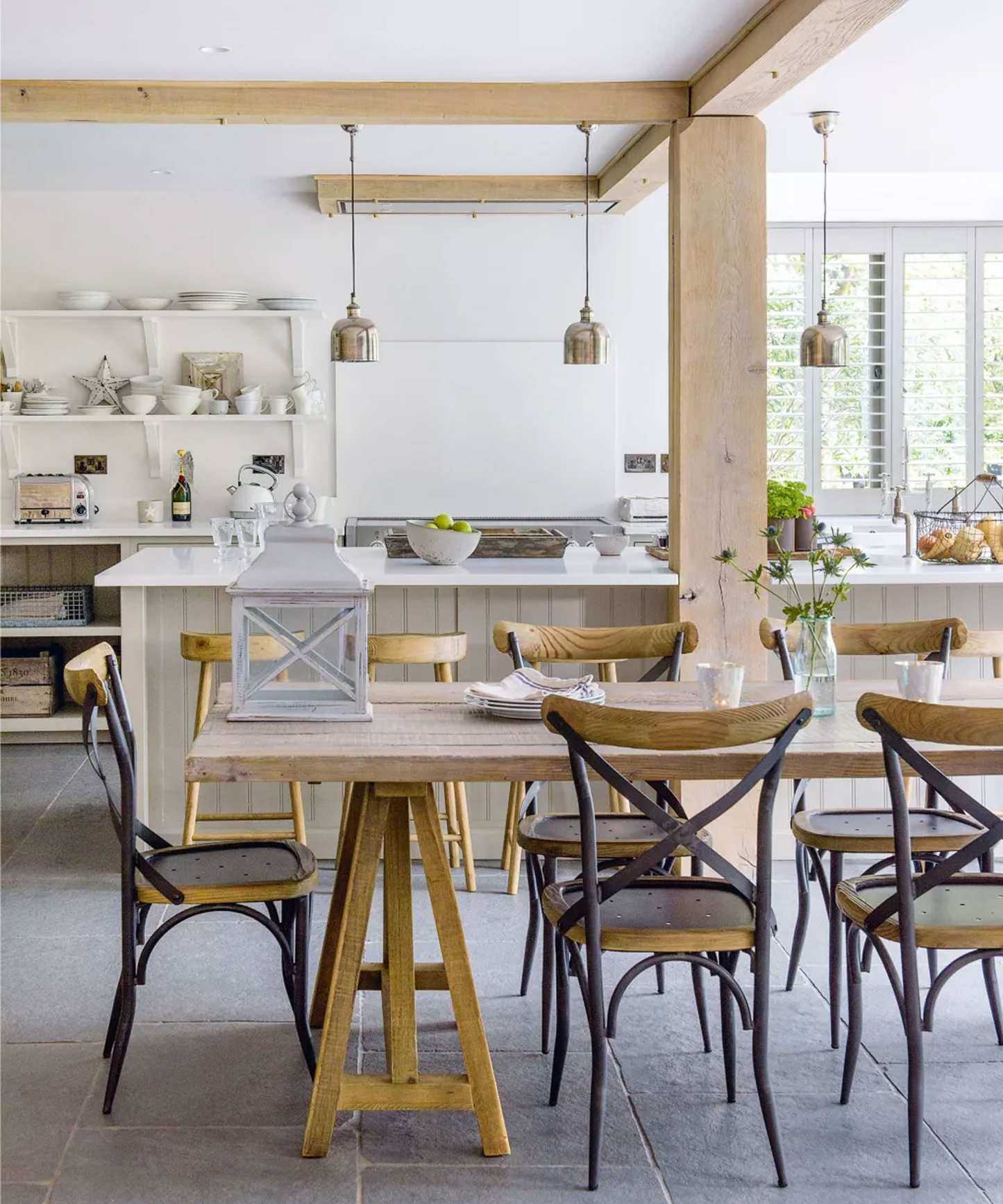 Large kitchen with wooden beams, large wooden dining table, kitchen island, wooden cabinetry, low hanging pendants