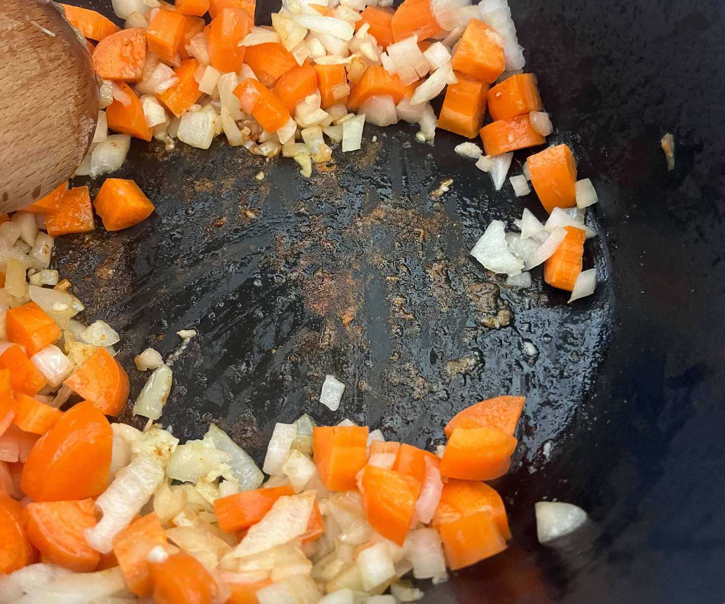 The fond on the base of a black Dutch oven filled with carrots and onions