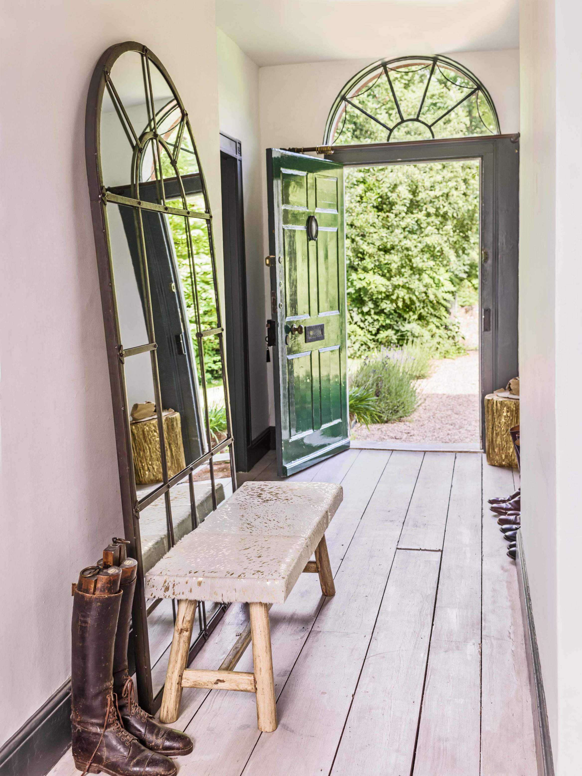 A large mirror leaning against a hallway wall, with a bench and wooden flooring.