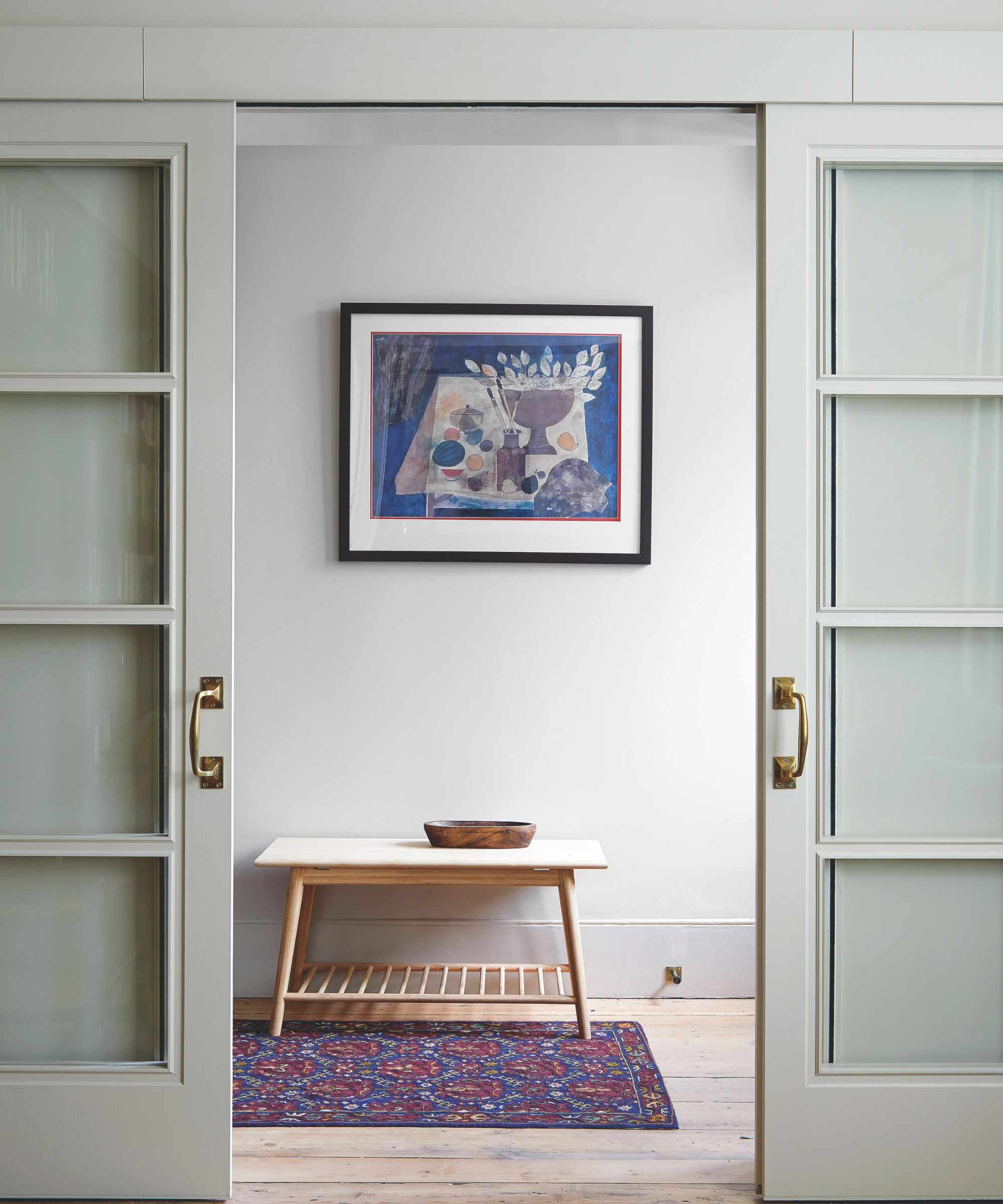 Minimal hallway with modern art on wall, sliding doors, wooden console and red and blue persian rug