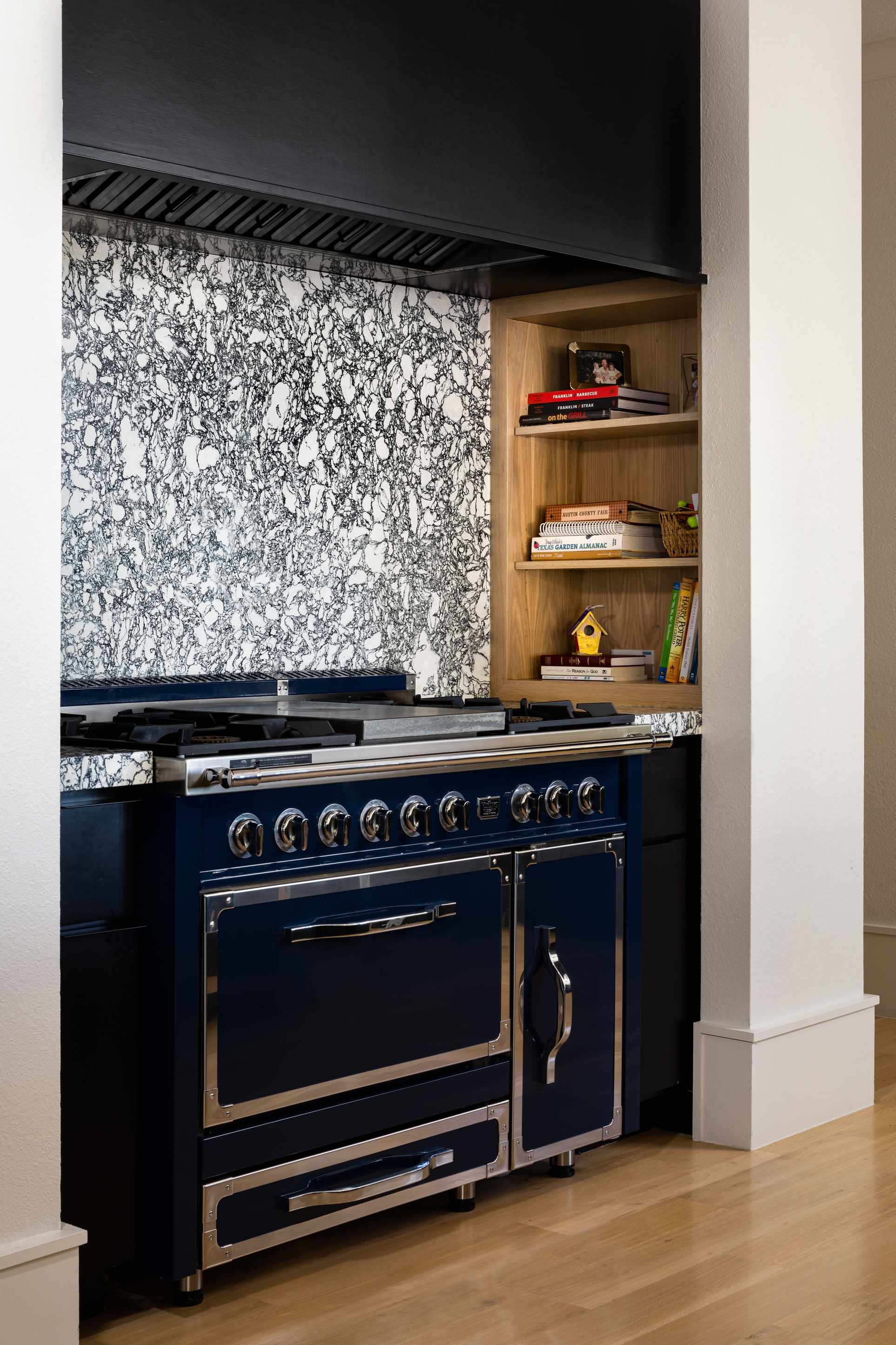 Stove with veined stone backsplash and niche with cookbooks
