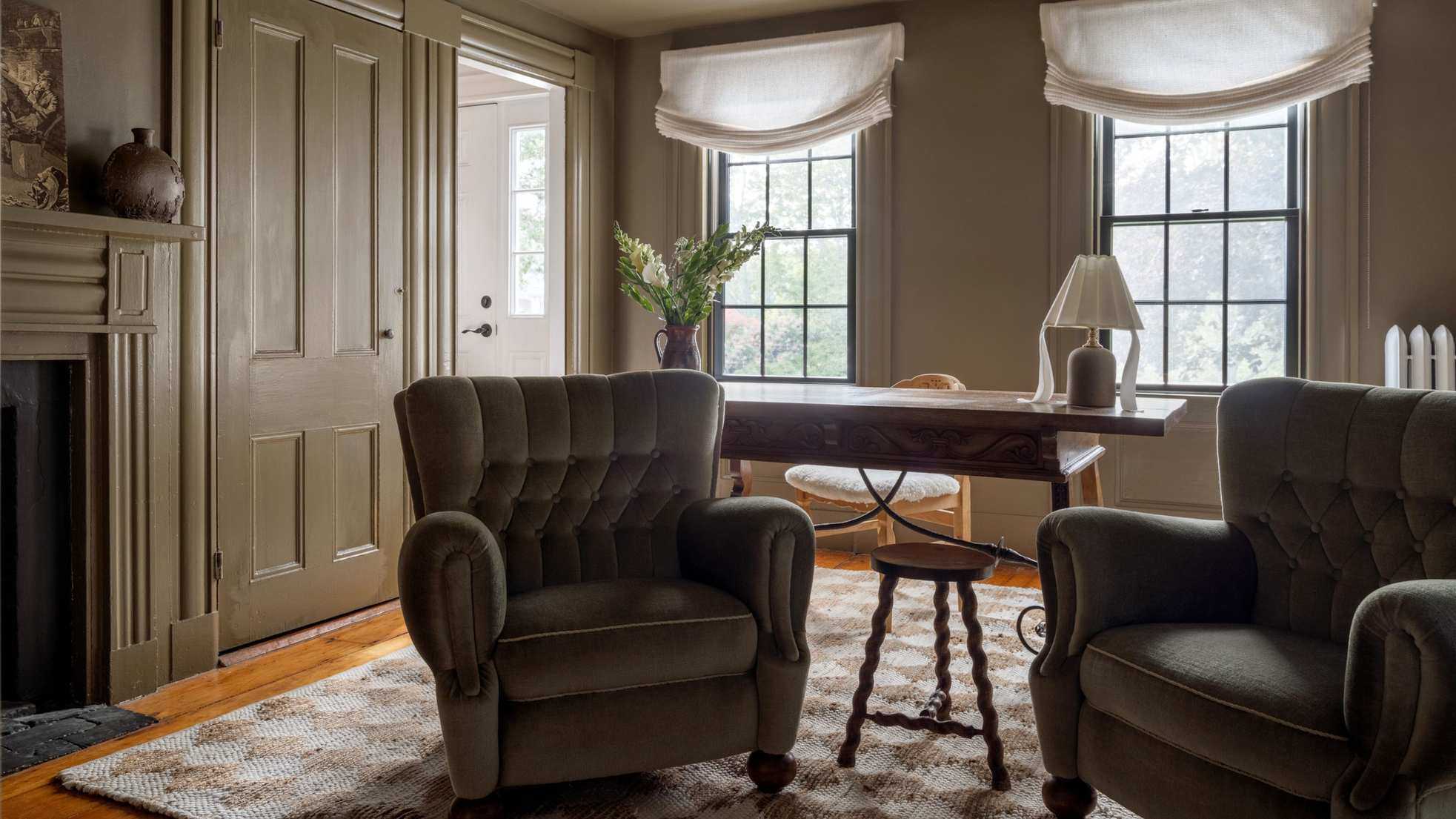 Muted earthy green living room with velvet armchairs, wooden floor, a desk and a chequered rug