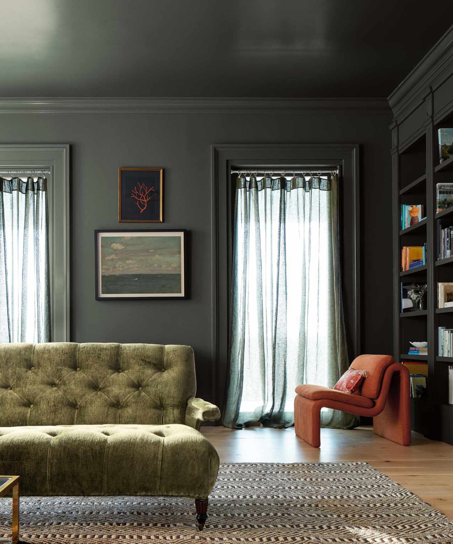 dark living room color-drenched with moody dark green paint, olive green sofa and red-pink accent chair