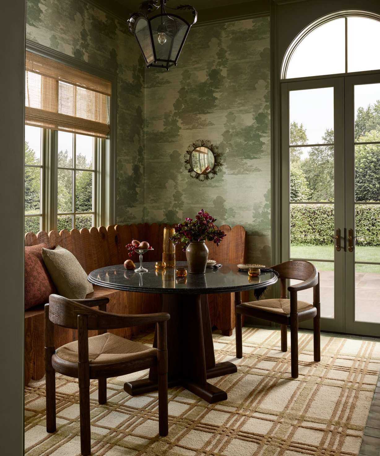 a dining nook with green wallpaper, a striped brown rug, a circular table, two chairs, and a built-in bench