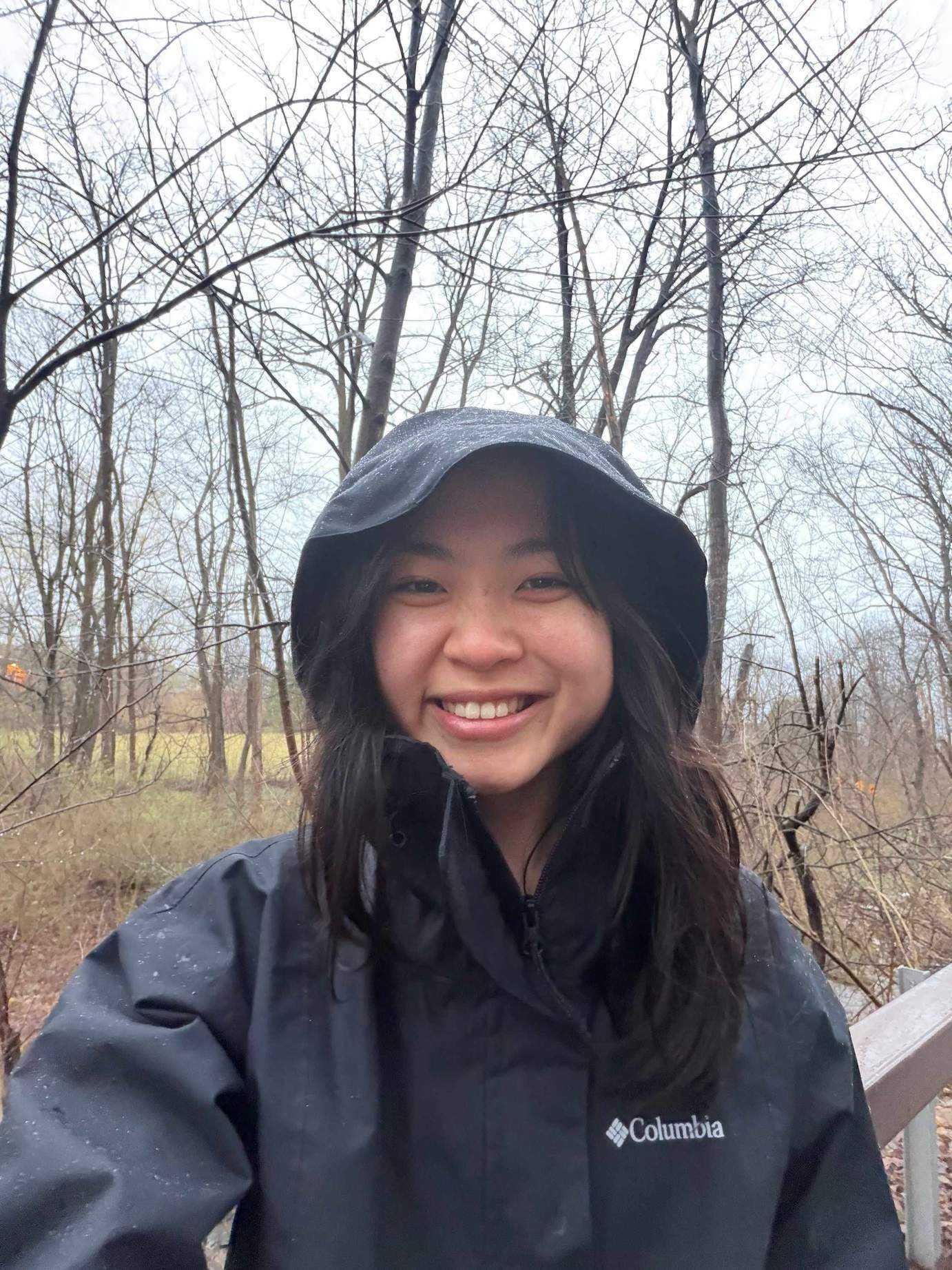 young woman wearing black anorak in a field with trees