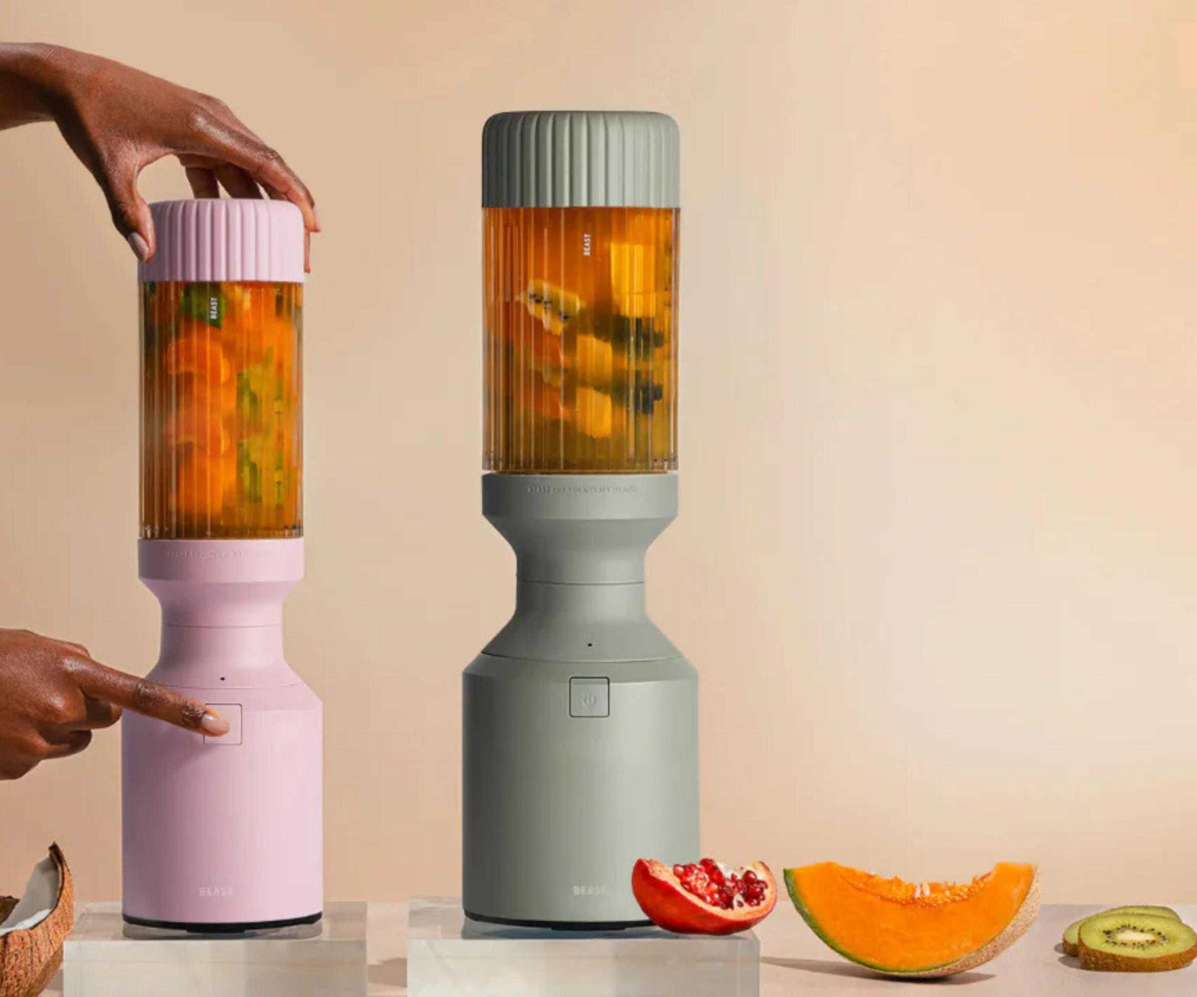 Two Beast blenders in mint and pink, blending tropical smoothies against a pale orange background
