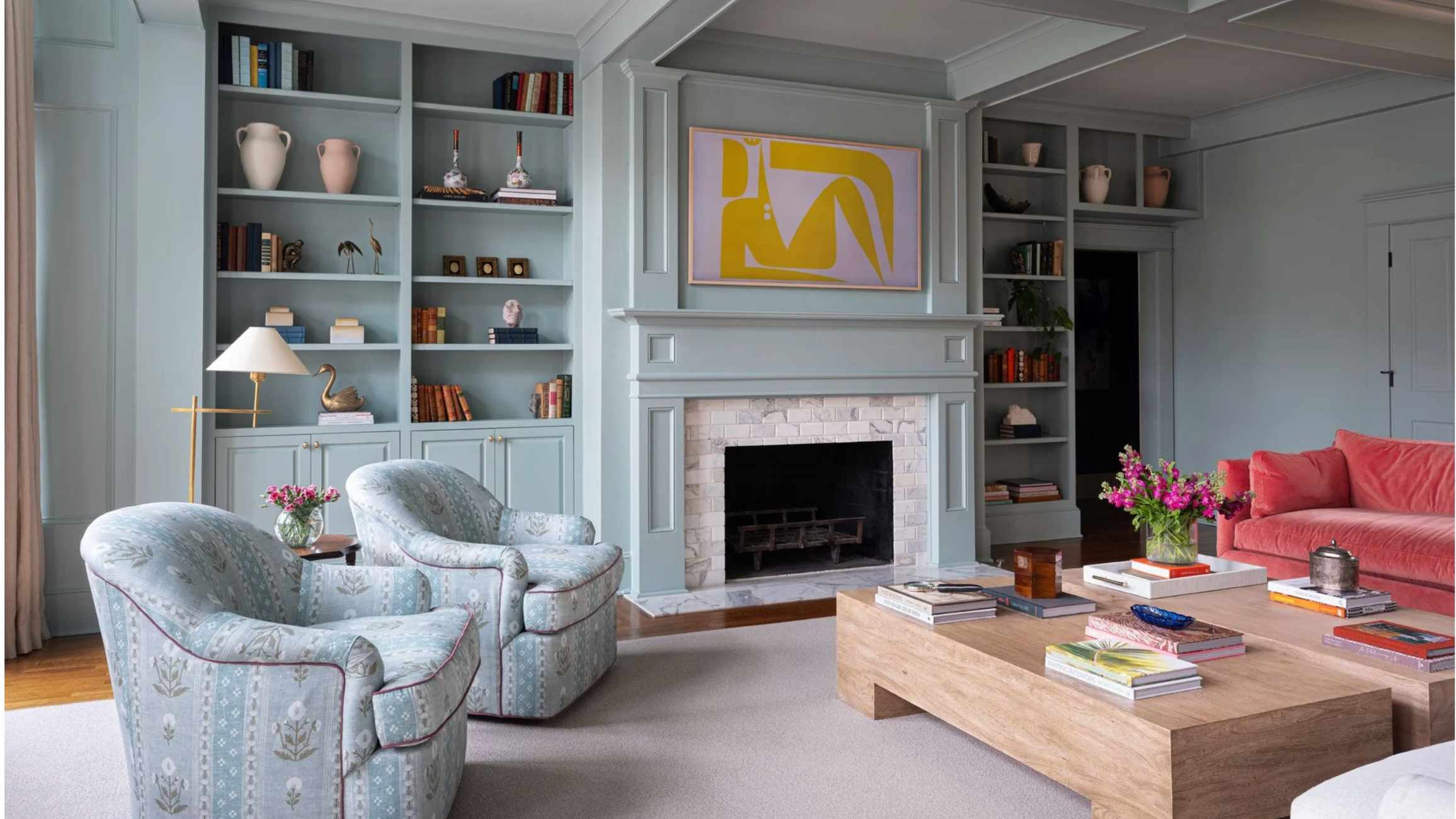 Pale blue living room with built in shelving and a bright coral sofa