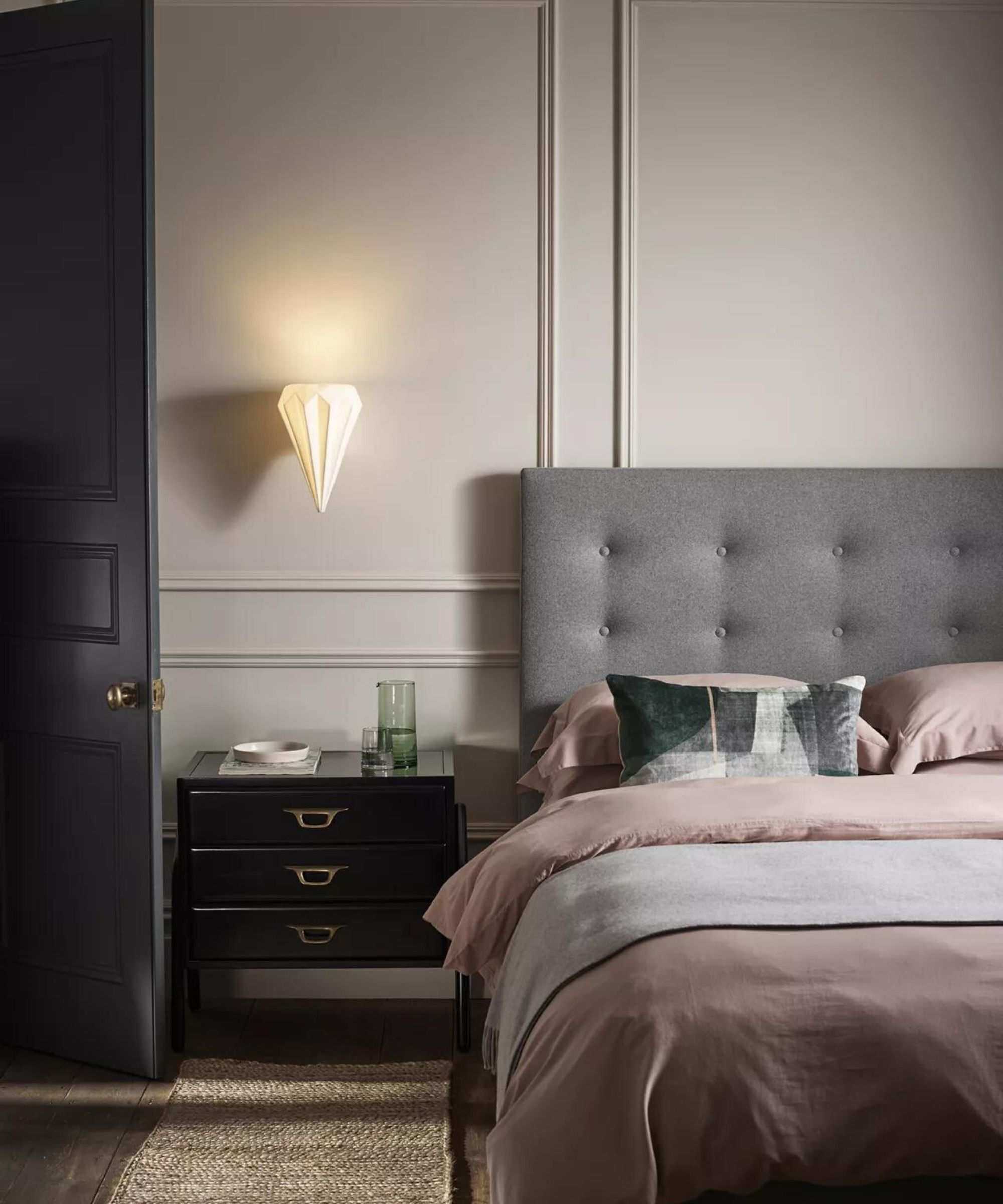 A padded headboard against a white, traditionally pannelled wall