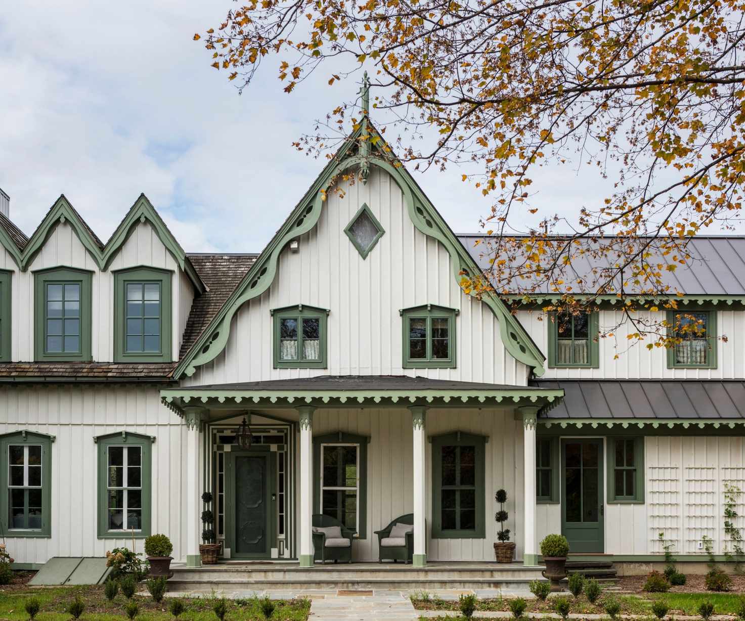 A historic home exterior with warm white wood, mid-toned green trim, and a porch with pillars.