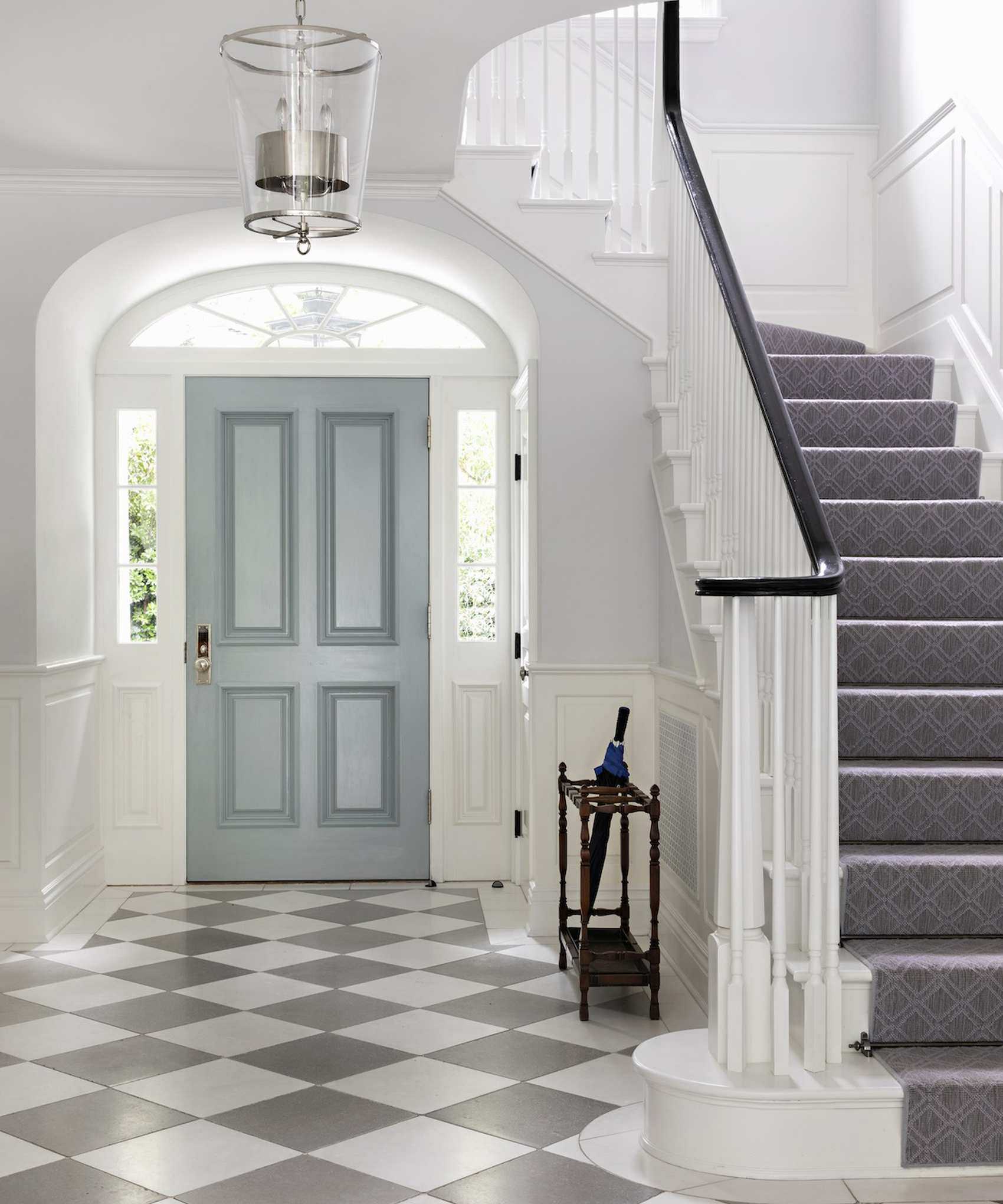 Gay and white checkered floor tiles and a sweeping white staircase.