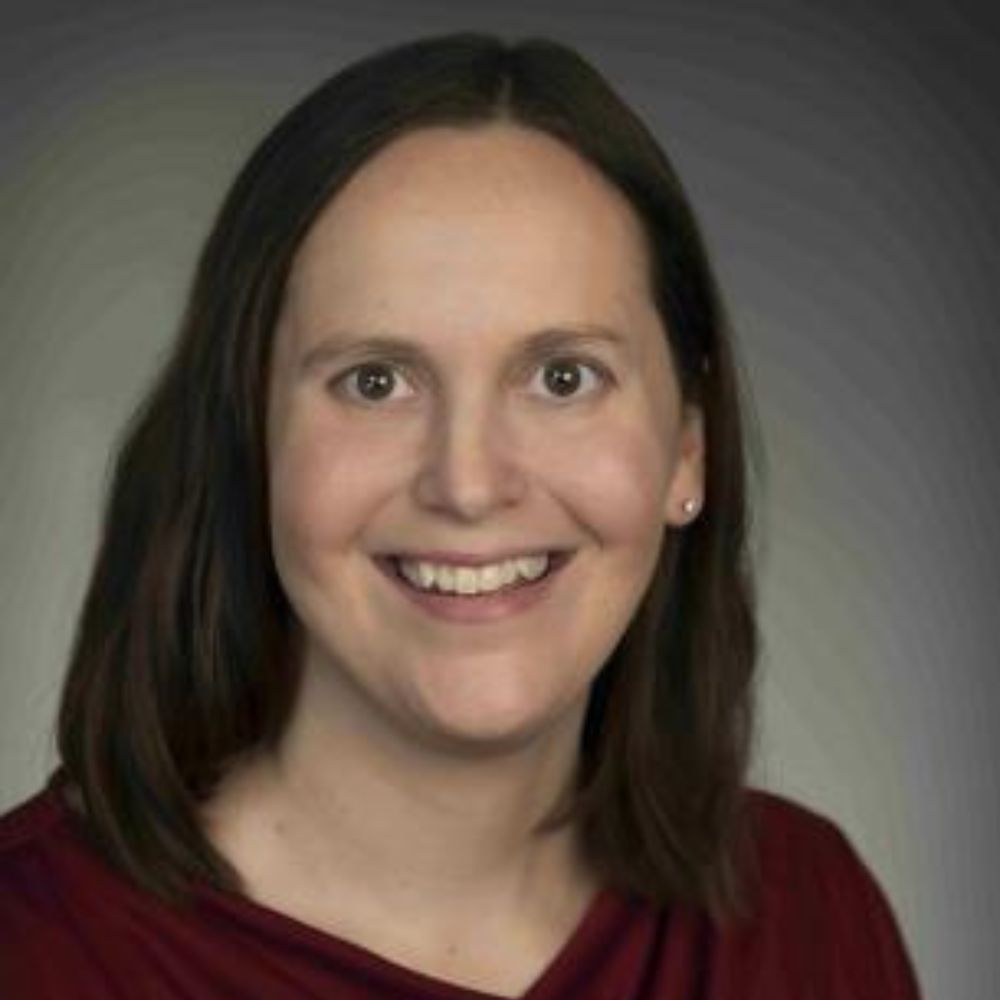 A headshot of Jessica Ek wearing a burgundy top against a grey background