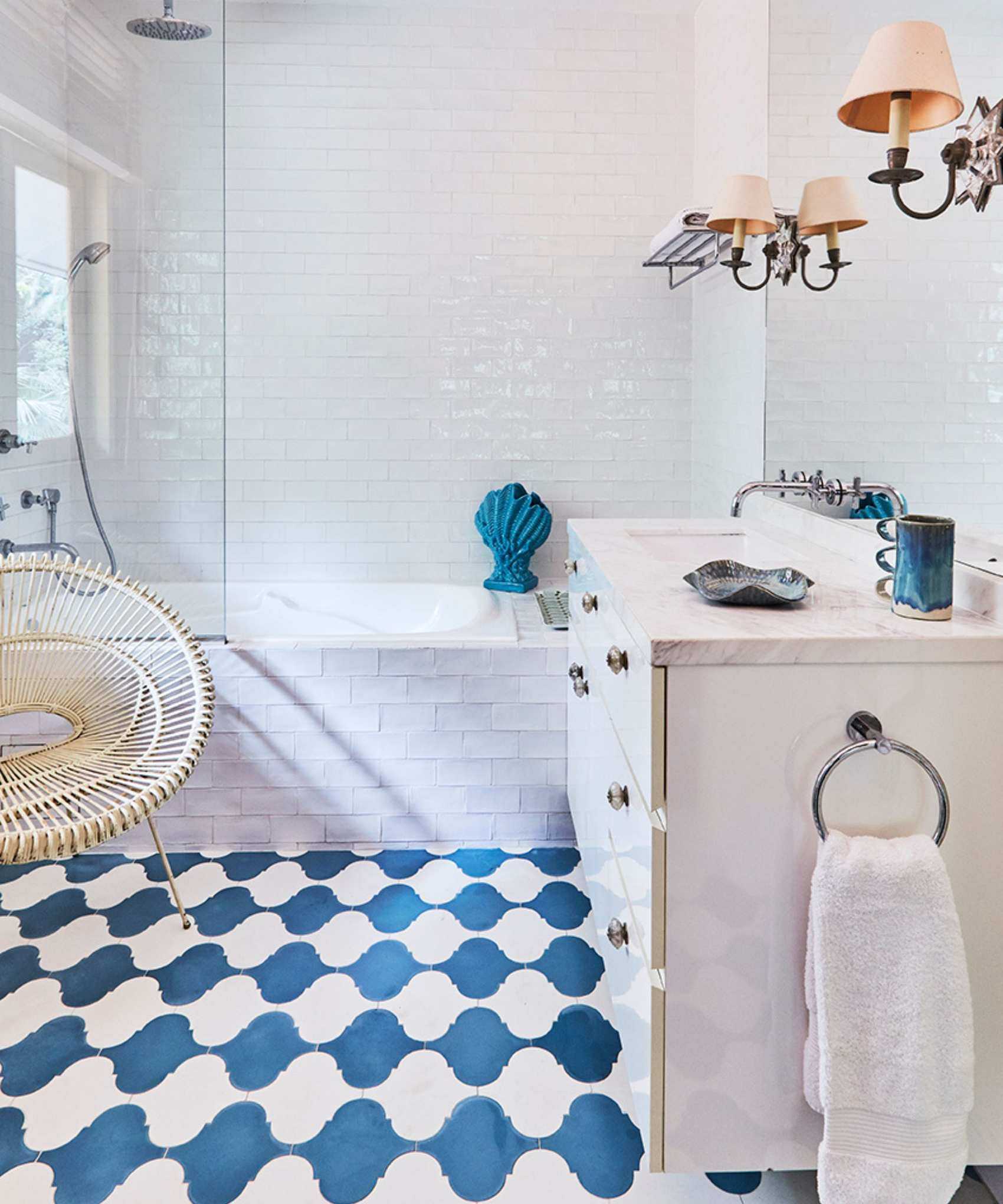 A white tiled bathroom with blue and white tiled flooring, a tiled bathtub, and a white cabinet with a white marble countertop and large mirror.