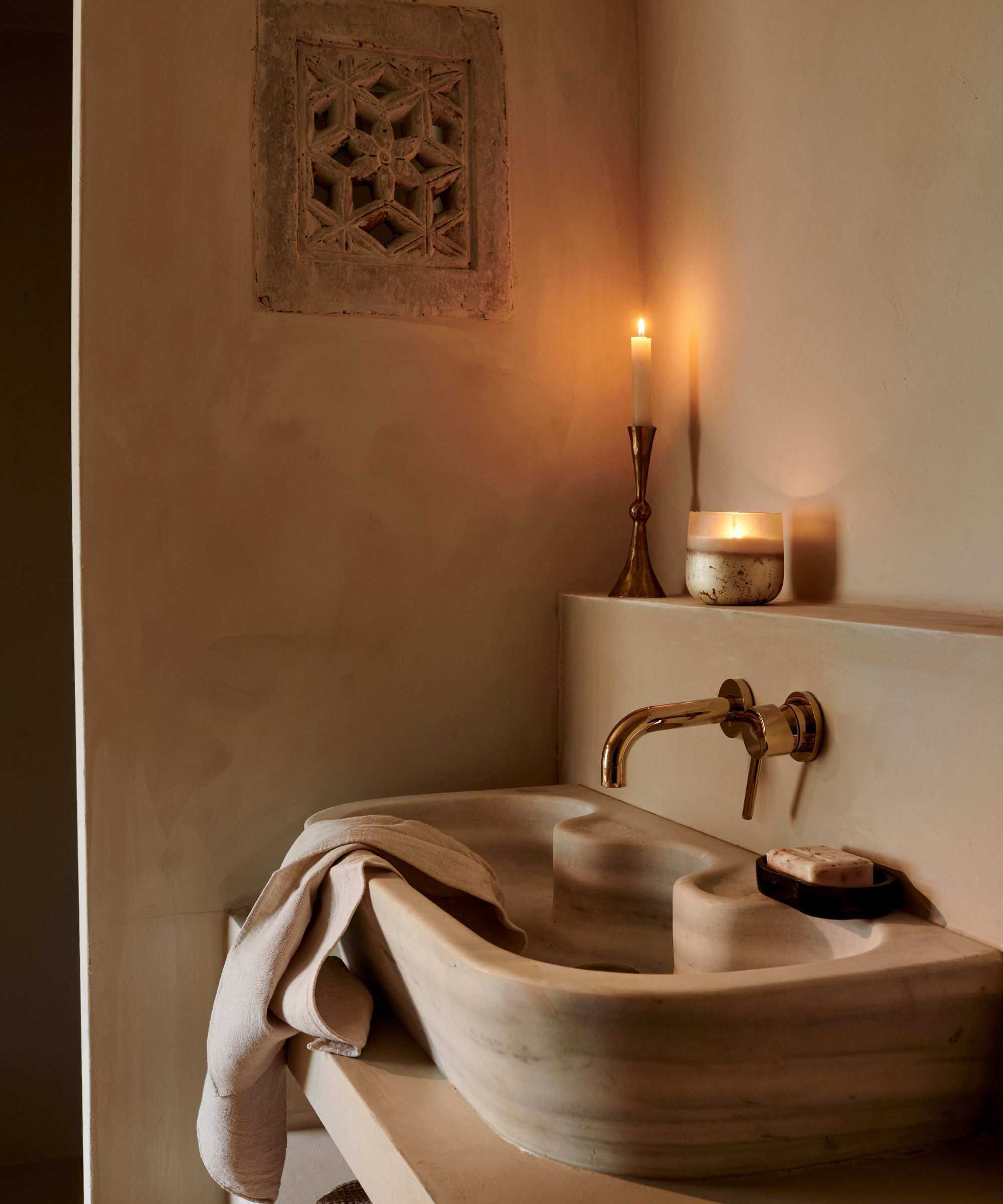 A carved stone sink in a paster-wall bathroom. A candle lit on the ledge above.