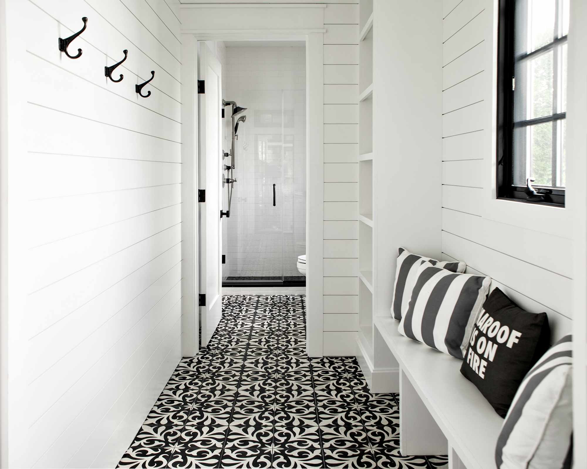 The entrance to a pool bathroom with black and white patterned tile floors and white shiplap walls.