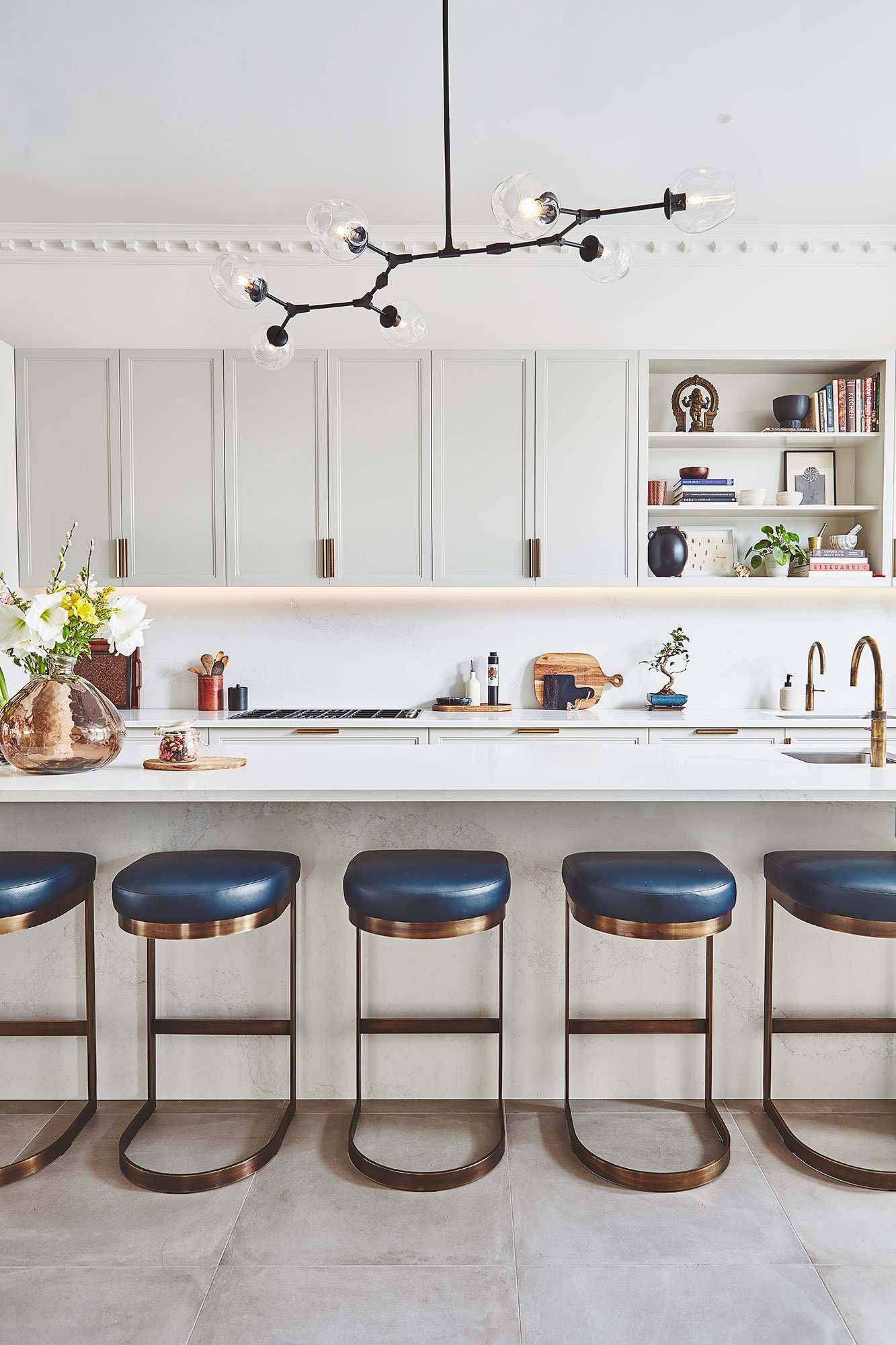 Black statement light in a white scheme with a row of blue and metal bar stools