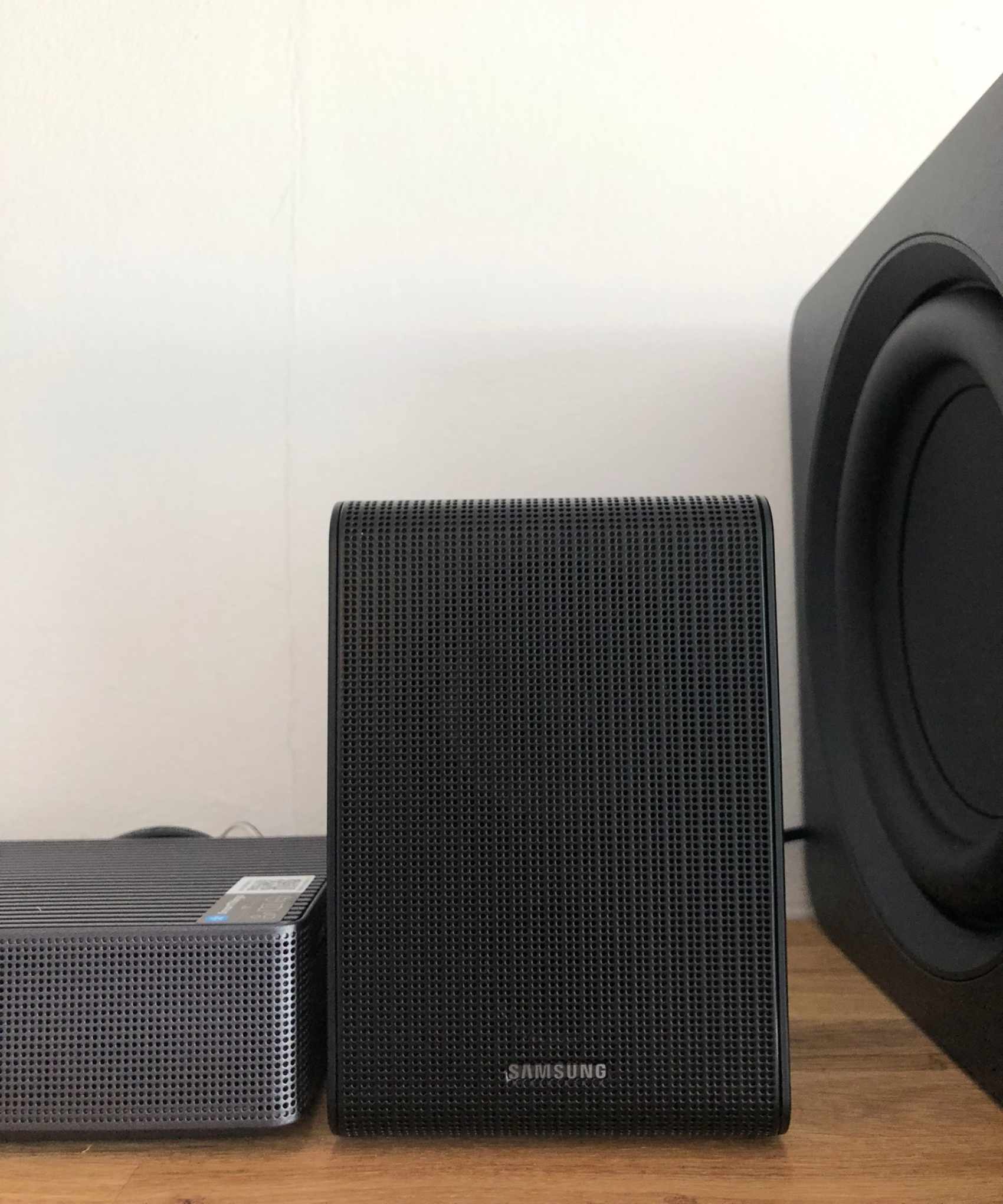 Closeup of surround speaker of Samsung HW-QS750F soundbar on wooden shelf in Dan Fauzi's home.