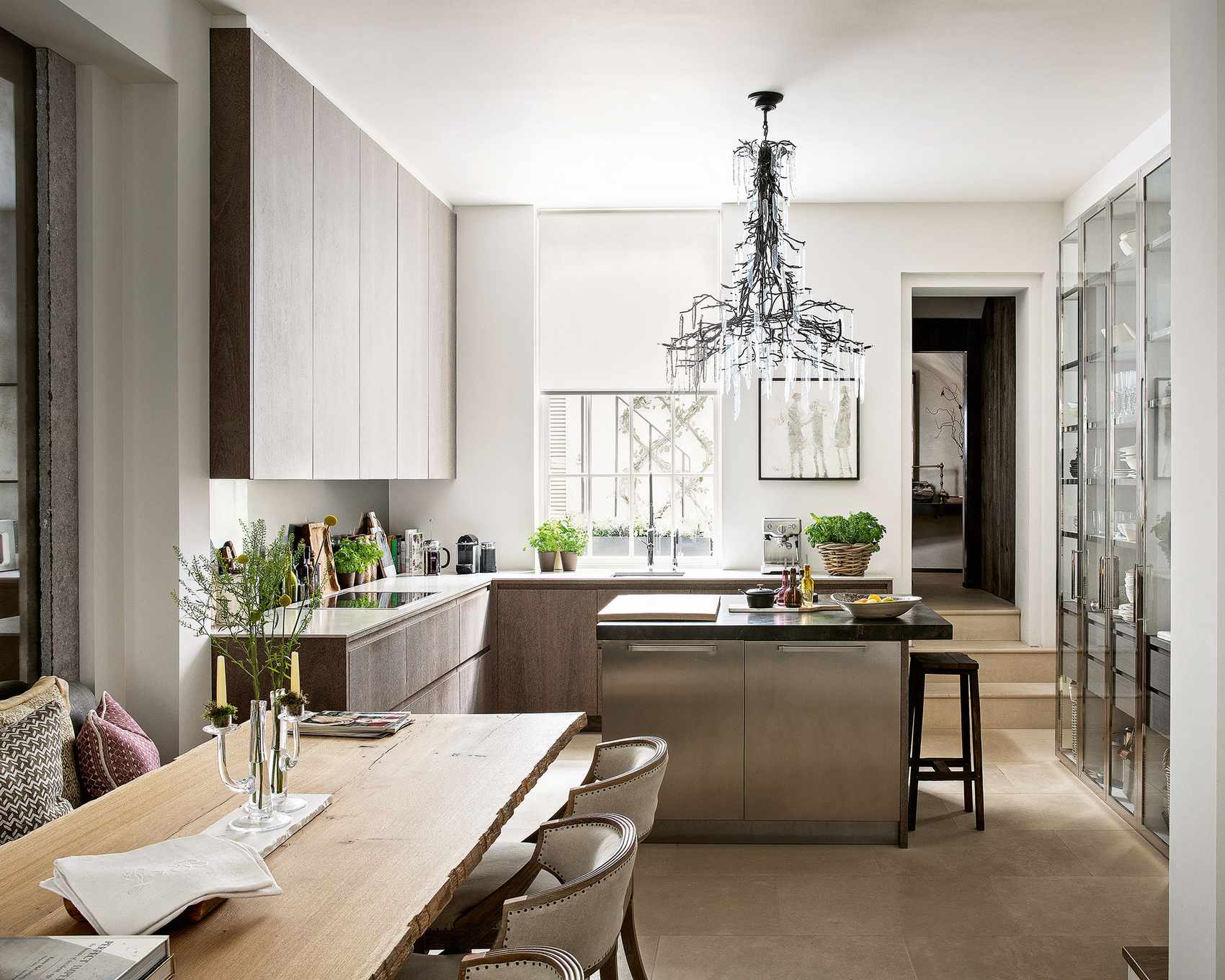 Grand chandelier over a chrome breakfast bar, with wooden cabinetry and a large dining table