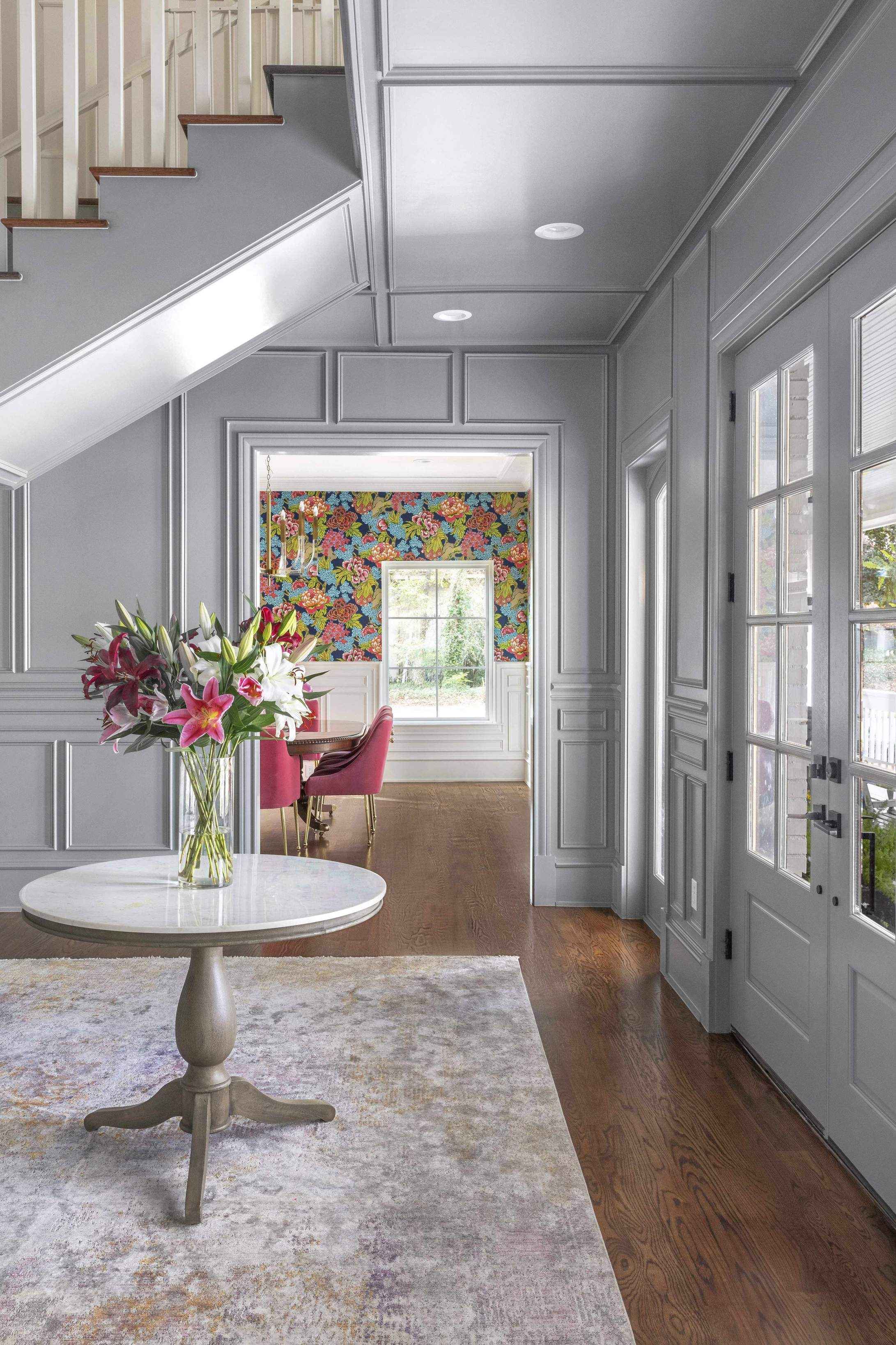 Hallway decor ideas with pale gray painted wood panelling and a round table with a vase of lilies.