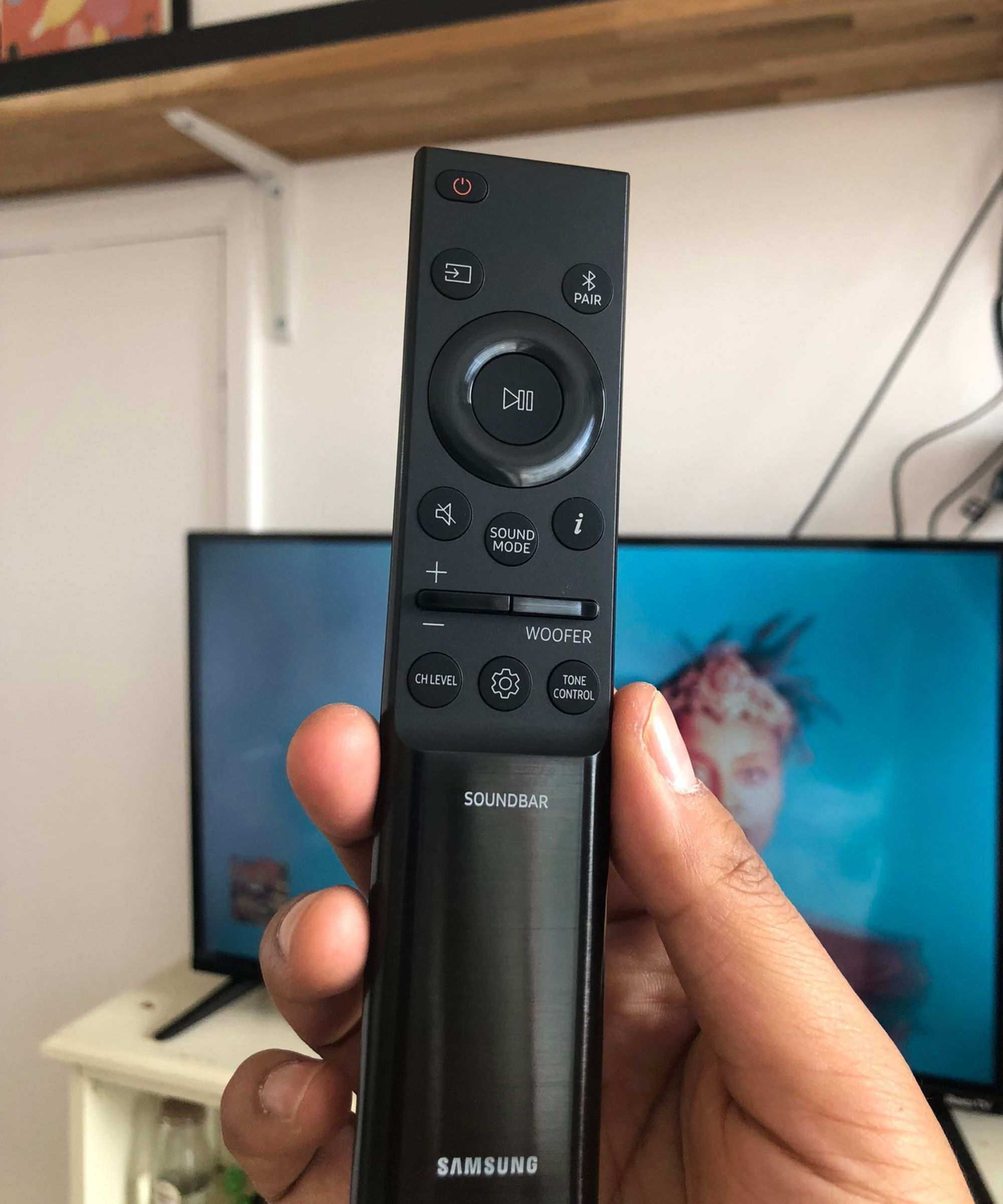Closeup of Samsung HW-QS750F soundbar remote held in front of TV in Dan Fauzi's home.