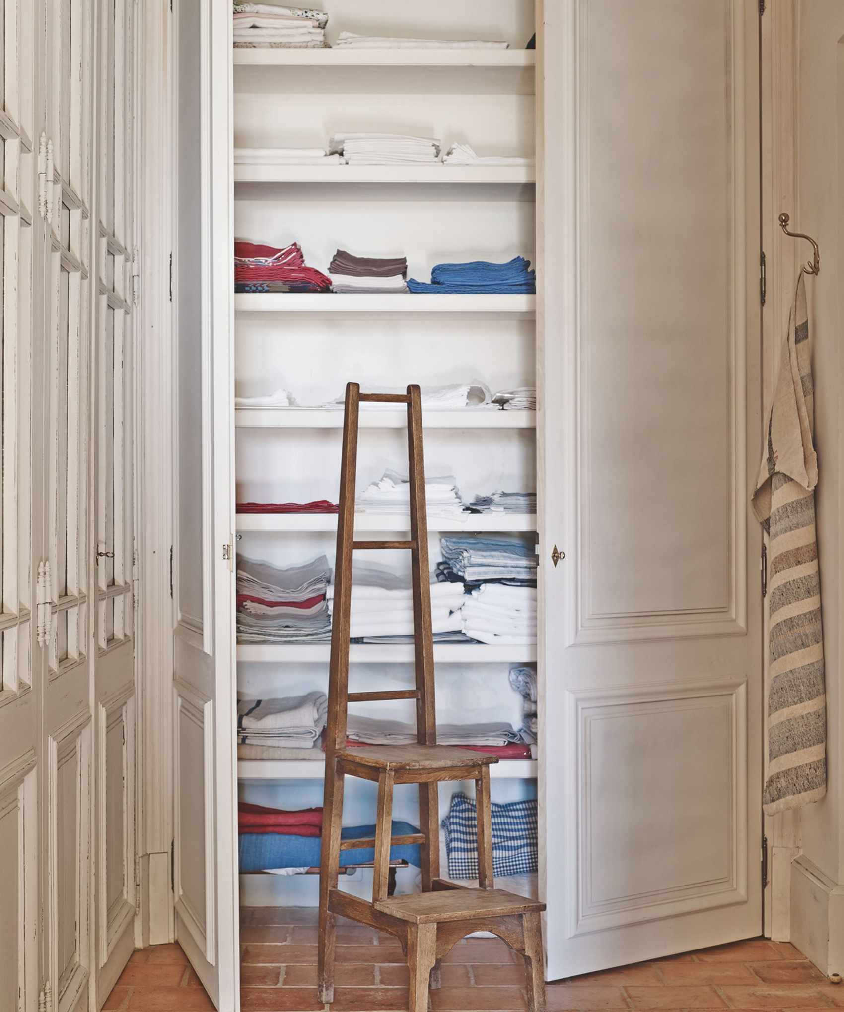 A white linen cupboard filled with folded laundry and a brown wooden ladder.