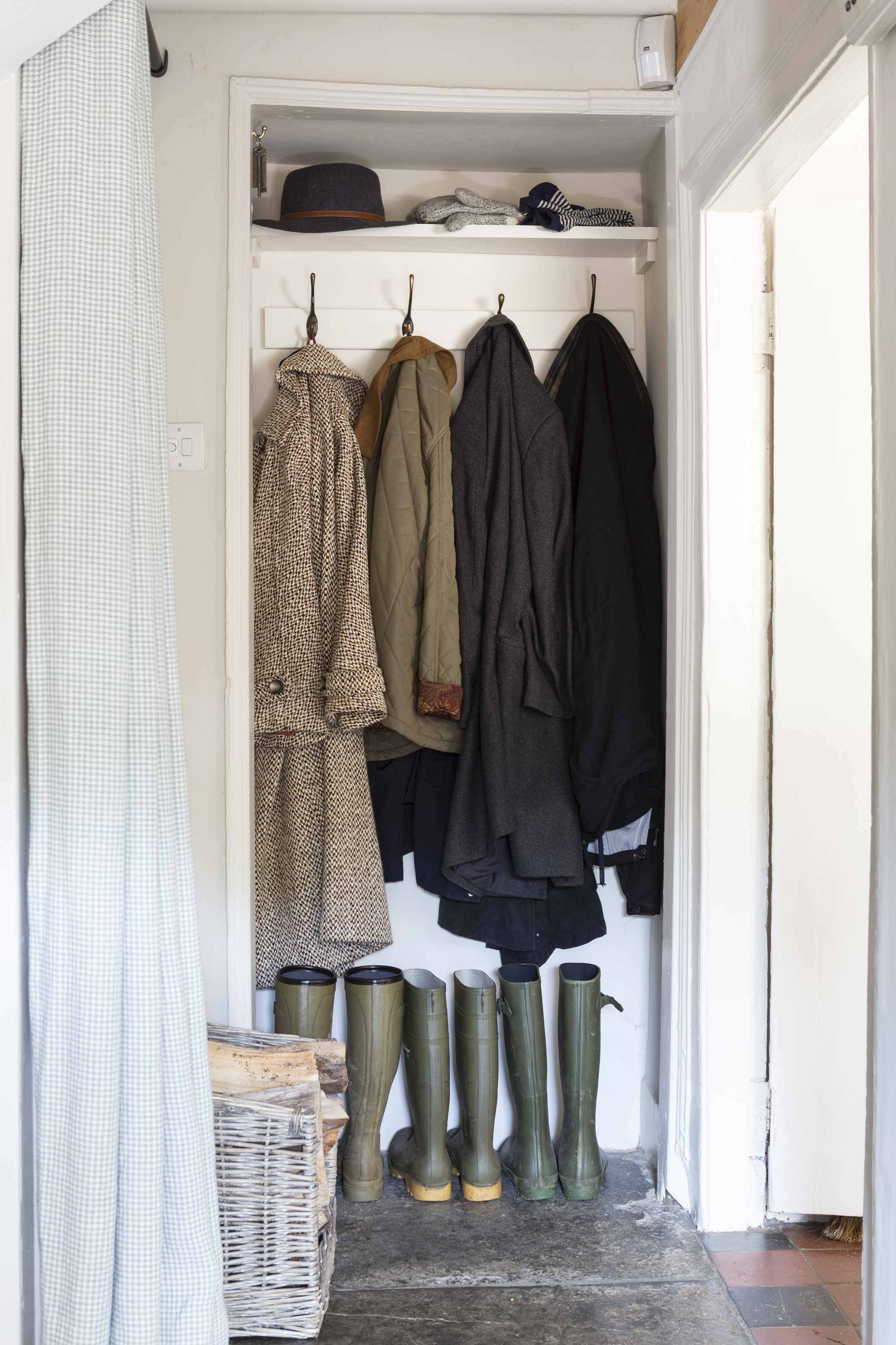 A small walk-in closet converted into a mudroom with wellies and coats