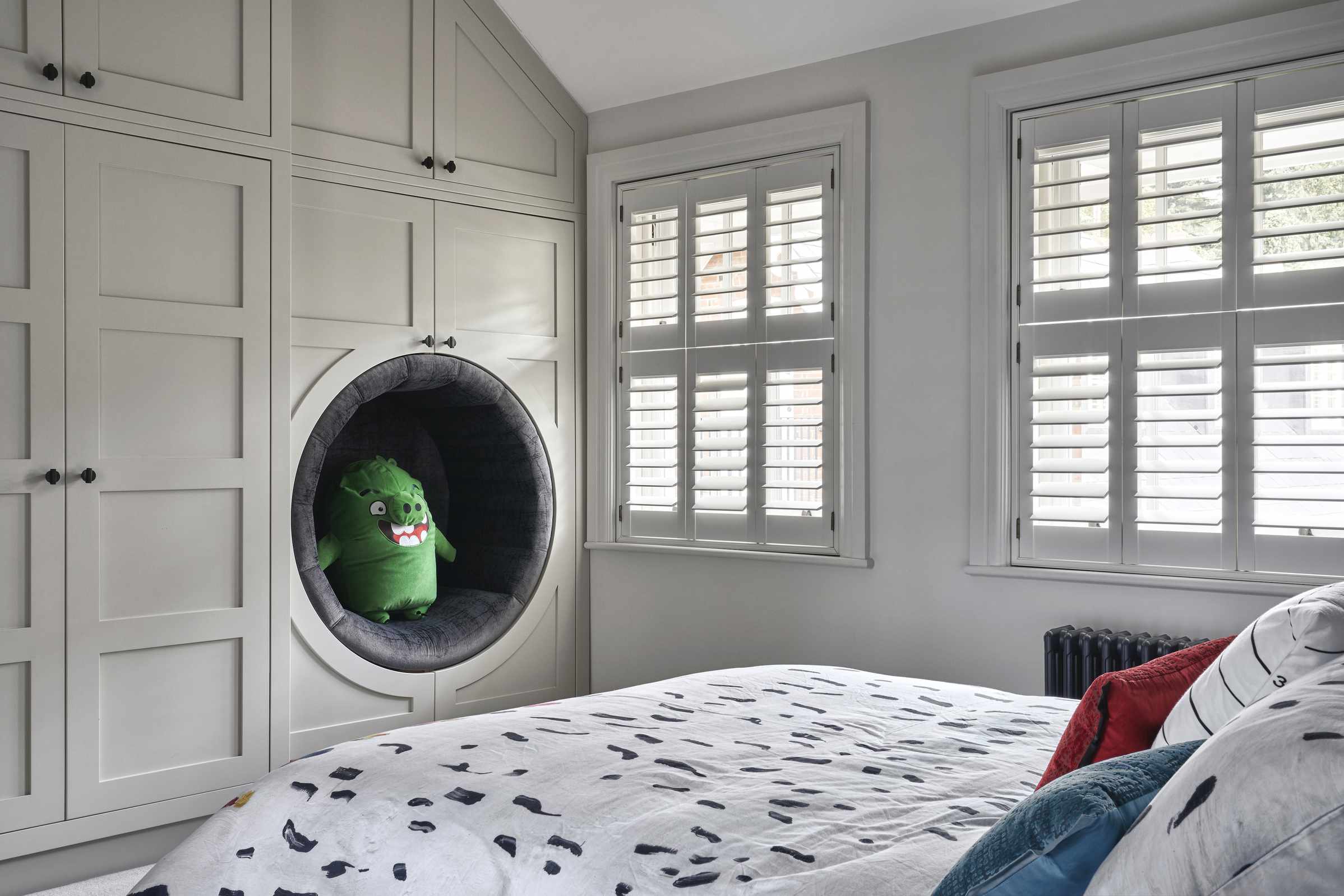 Child&rsquo;s bedroom with bed with patterned linen, built in wardrobes and reading nook and shutters on windows