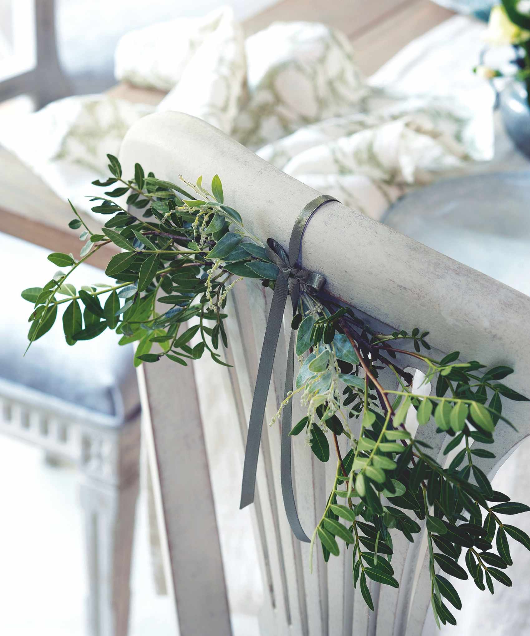 greenery tied to the back of a white dining chair with a grey ribbon