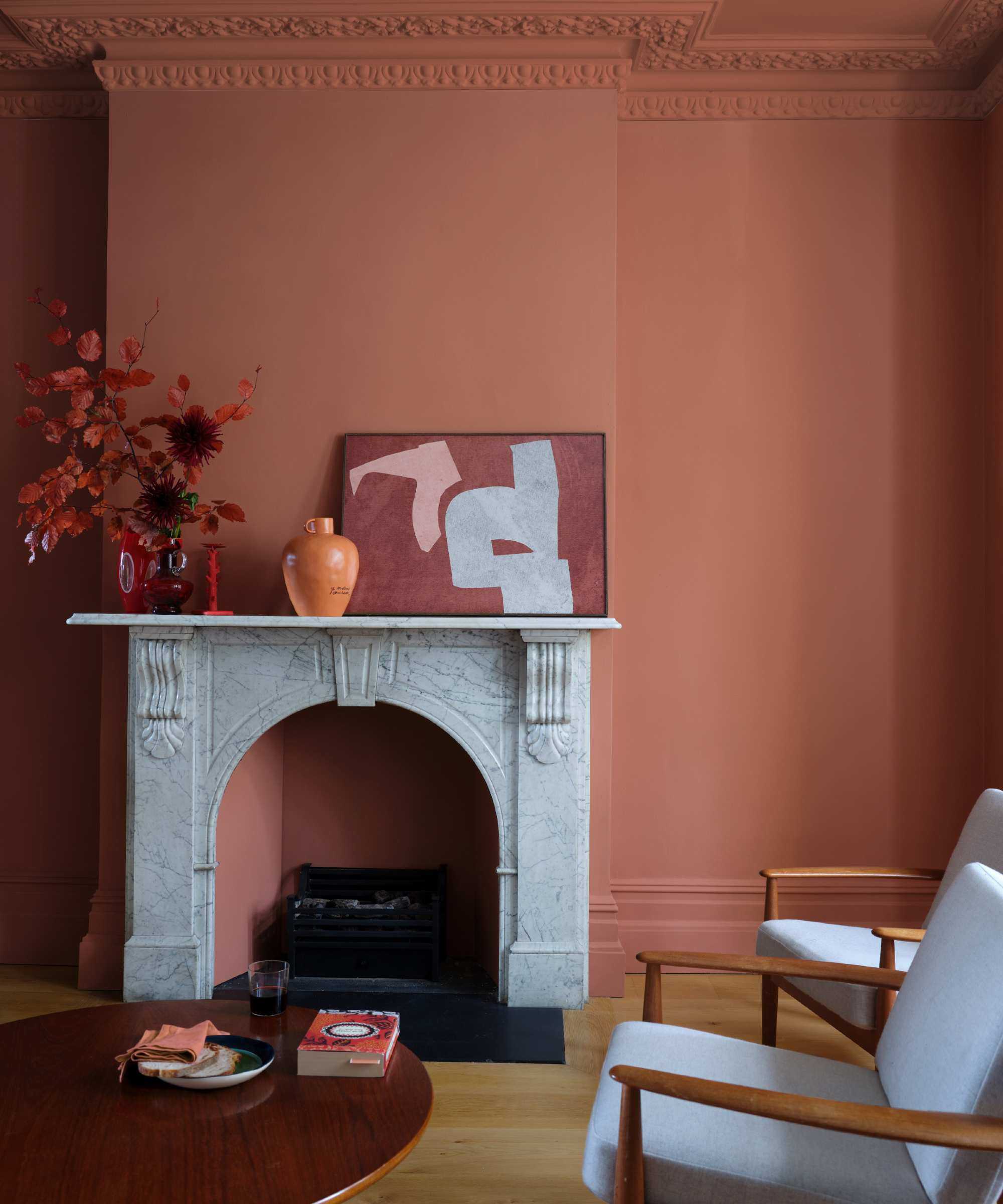 terracotta living room, color drenched walls, window and skirting, hardwood floor, marble fire surround, artwork, round coffee table, two wood upholstered armchairs, vases, side table, Farrow &amp; Ball