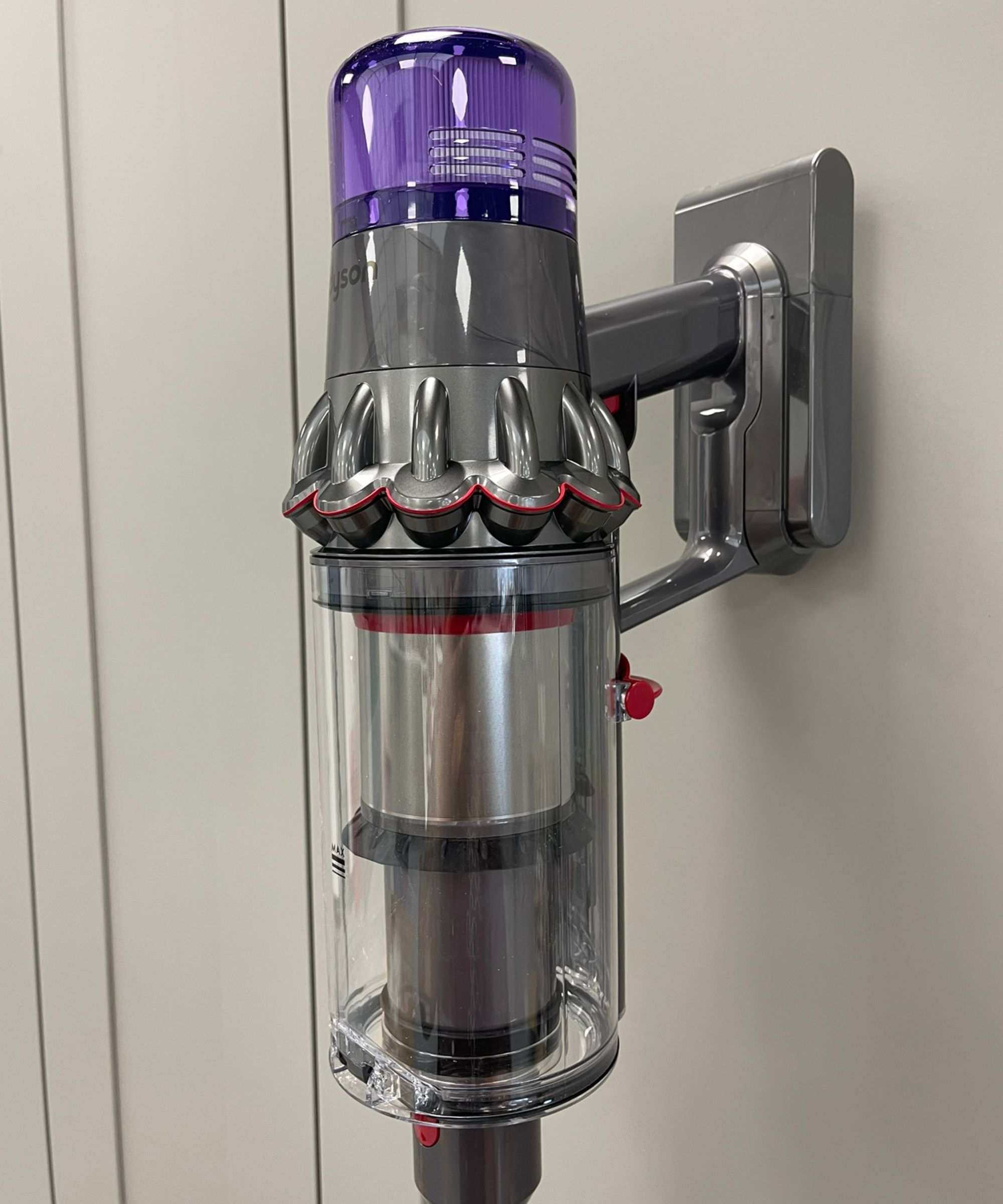 Dyson V11 cordless vacuum leaning on gray cabinet doors, in reflective gray and purple colorway.