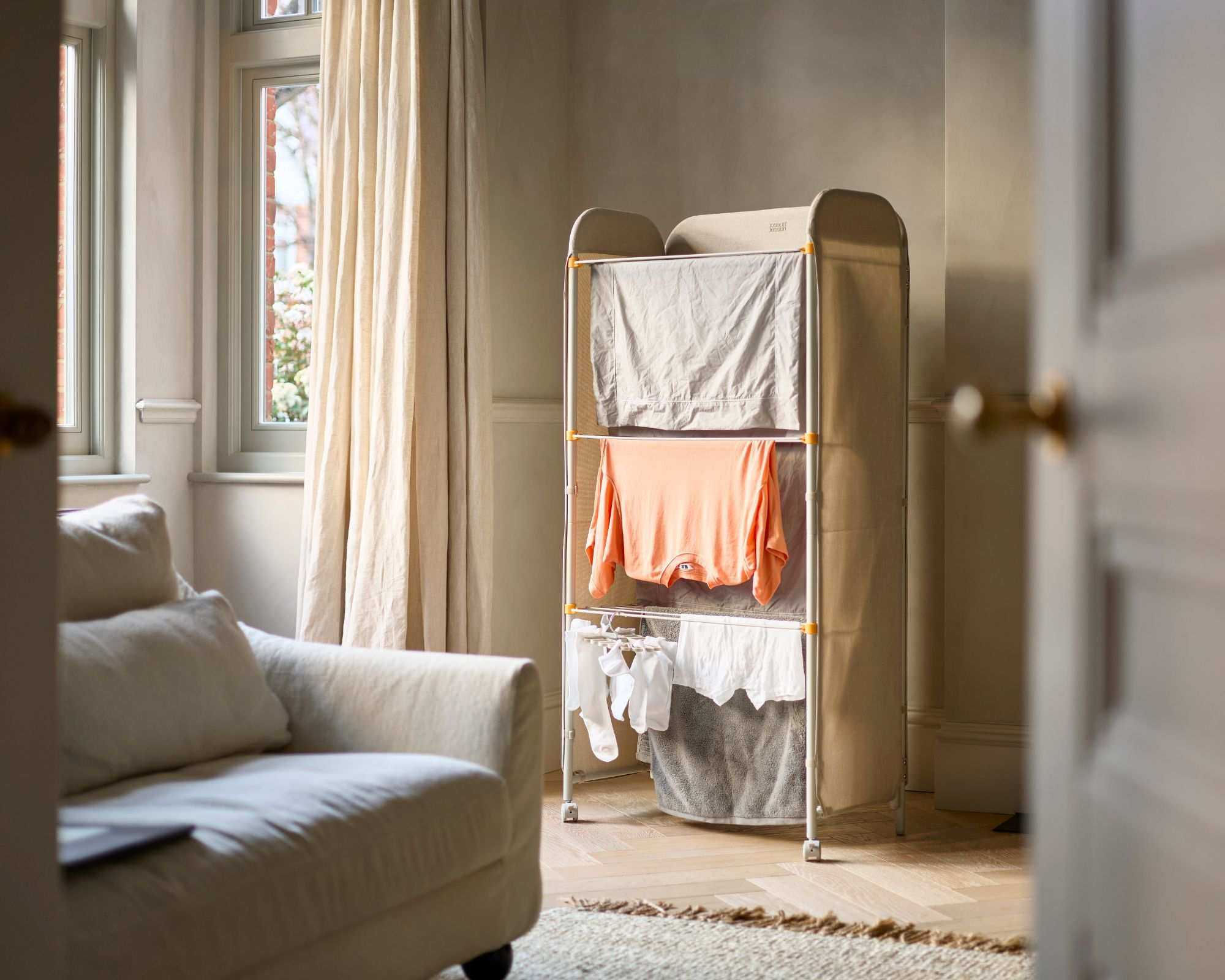 An image of the Eclipse&trade; 3-tier Ecru Clothes Drying Rack With Screen in a living room with clothes