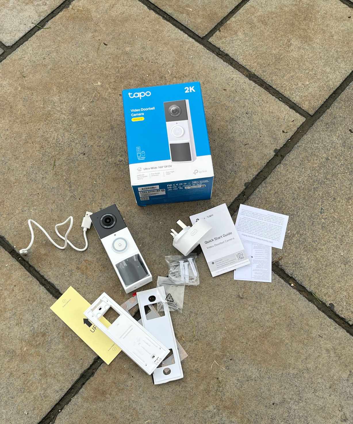 Every part of the Tapo D210 Video Doorbell kit unboxed on tiled concrete floor.