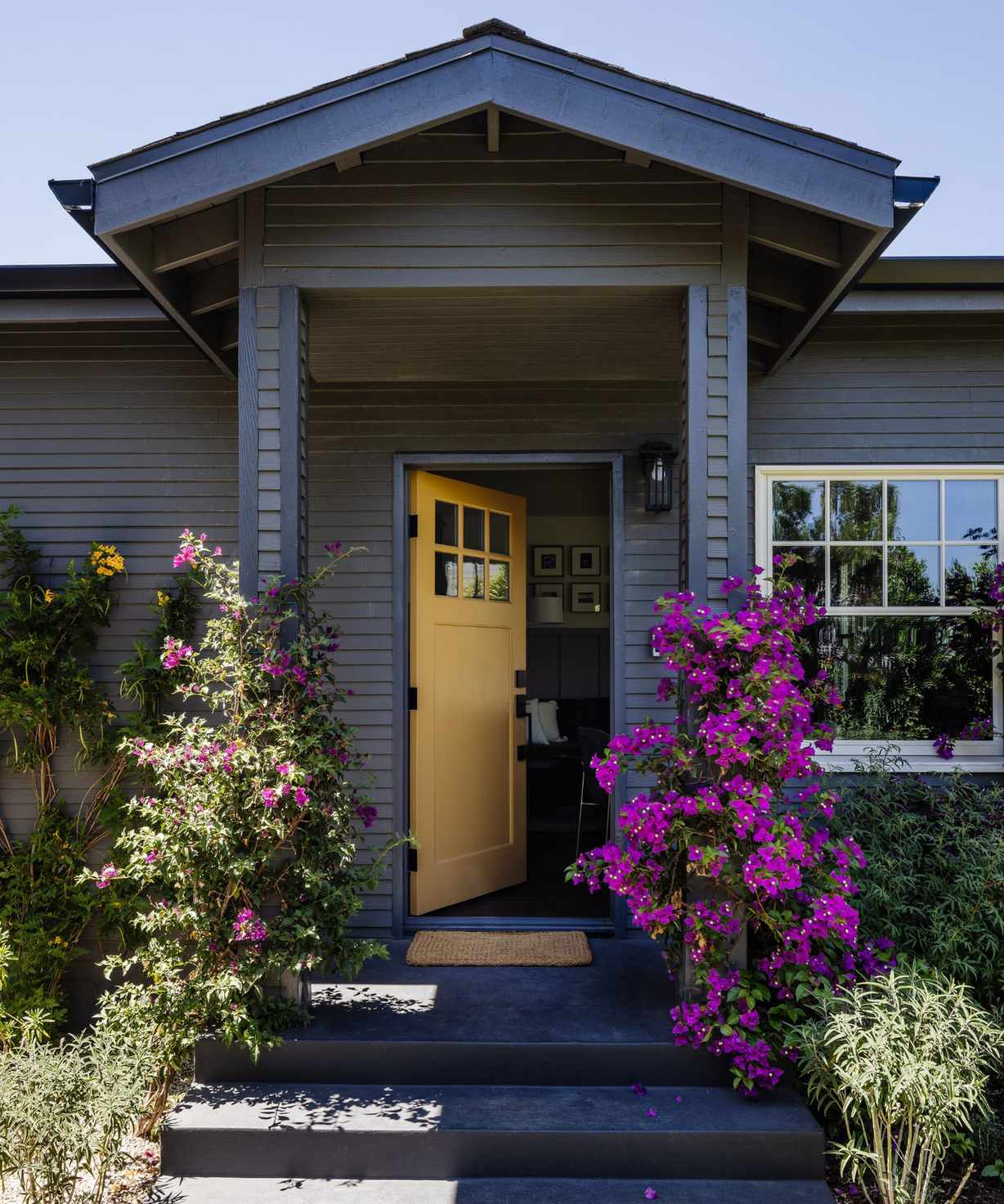 House with grey wood panelling, yellow front door and purple flowers