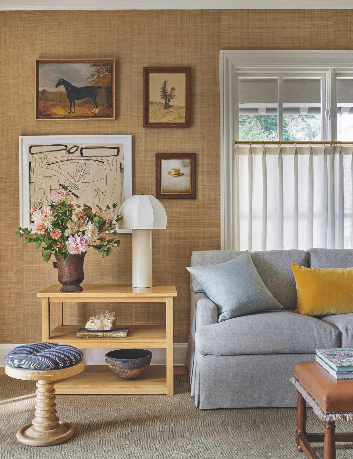 Living room with pale gray sofa and beige grasscloth walls with a small gallery wall and pale wooden side table